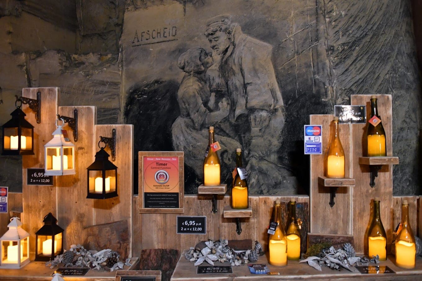 Lit lanterns stand on wooden crates below a carved figure inside the Fluweelengrot in Valkenburg.