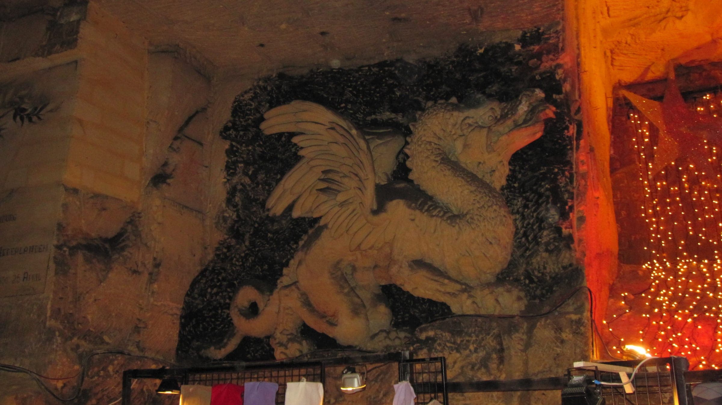 A winged dragon carved into the marl wall of the Gemeentegrot in Valkenburg looms over a market stall.