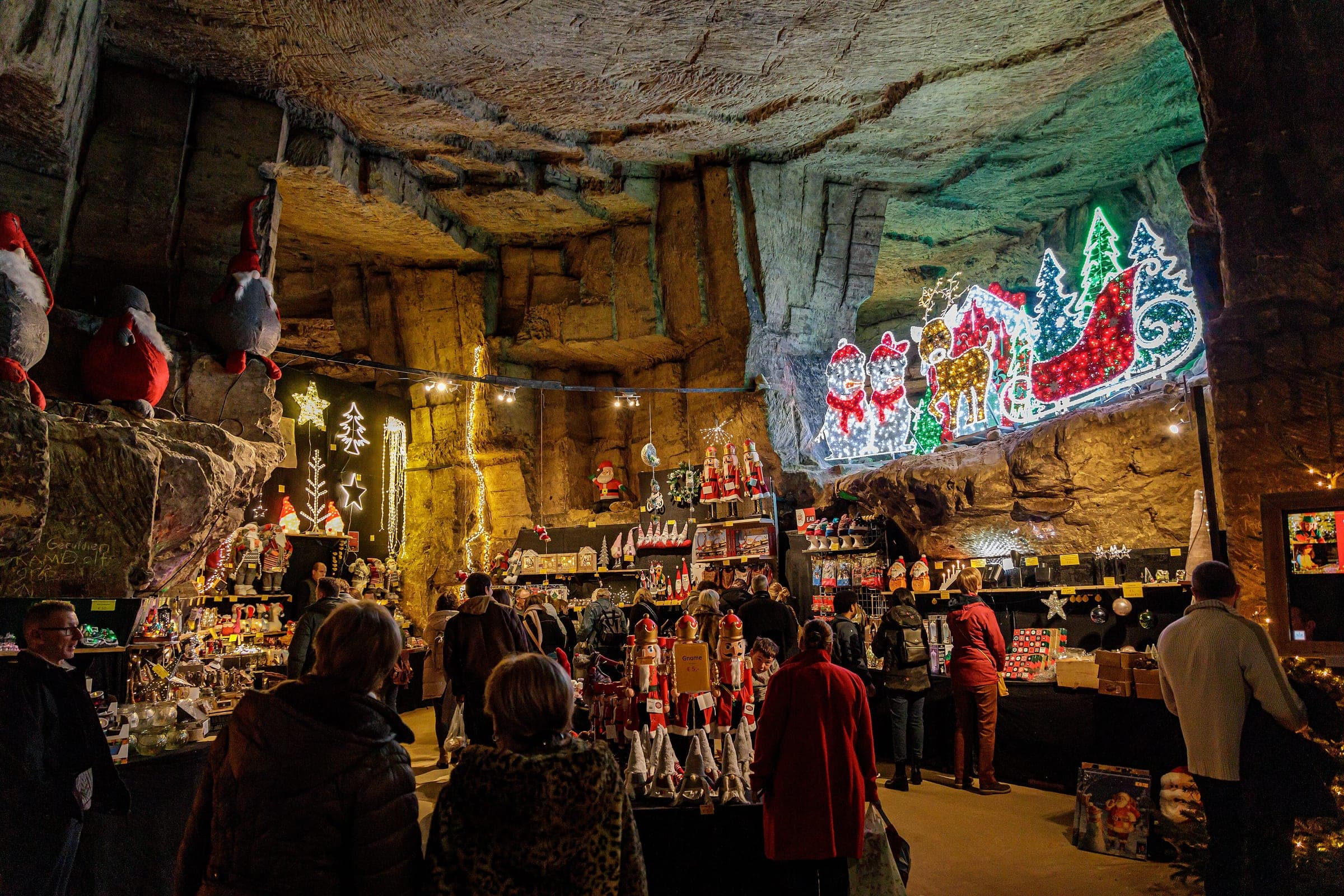 Shoppers browse lit stalls under the carved marl ceiling of the Gemeentegrot Christmas market in Valkenburg.