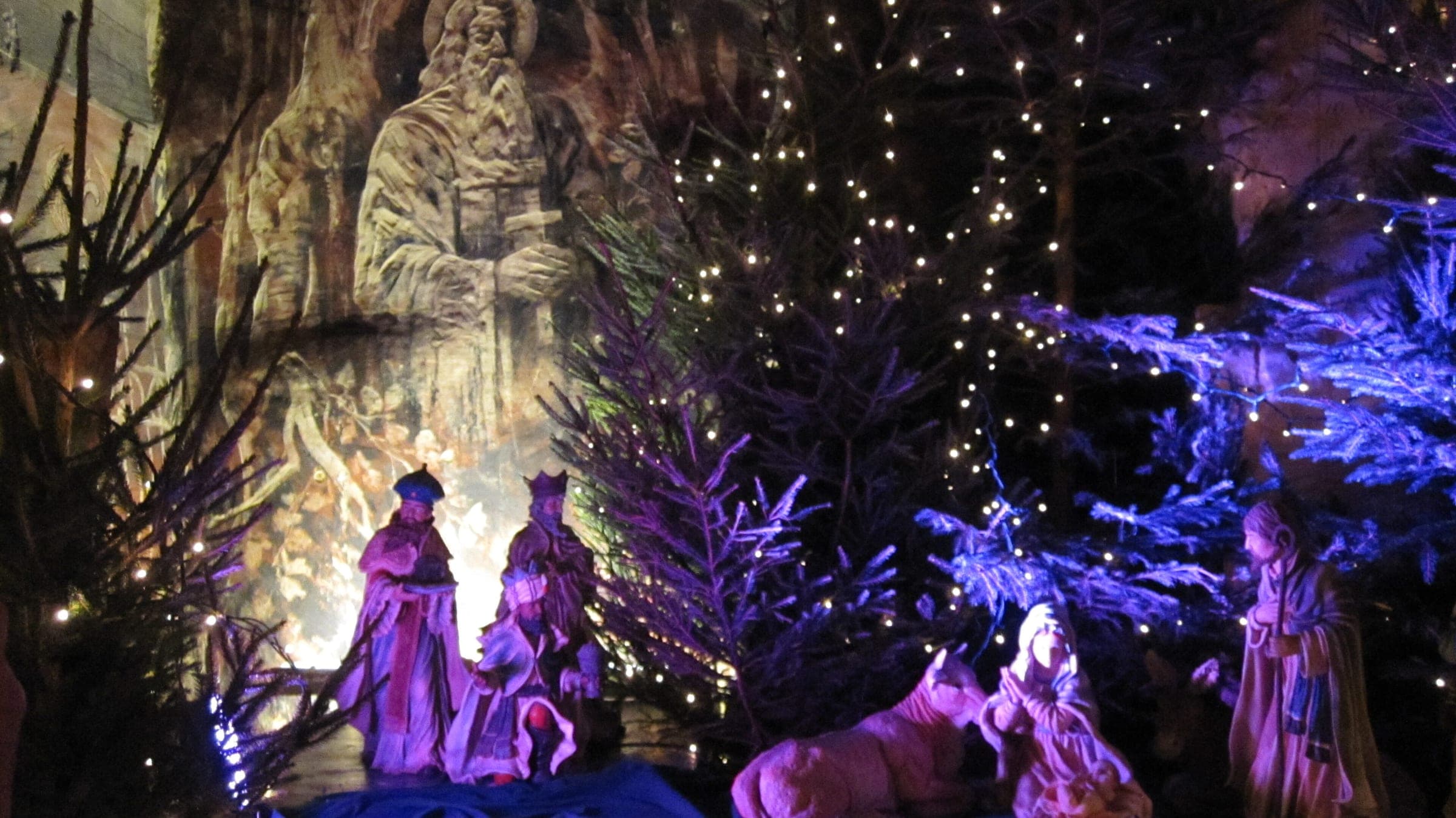 Coloured light falls on a nativity scene and a carved figure on the marl wall of the Gemeentegrot in Valkenburg.