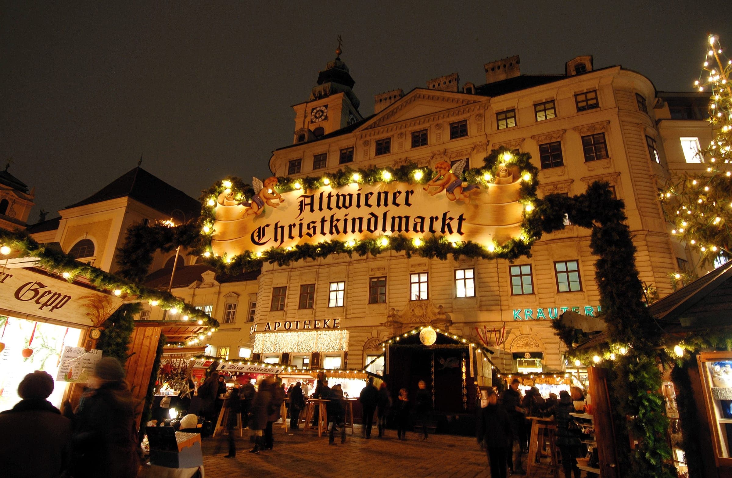 The lit Altwiener Christkindlmarkt arch spans the stalls on the Freyung in Vienna at night.
