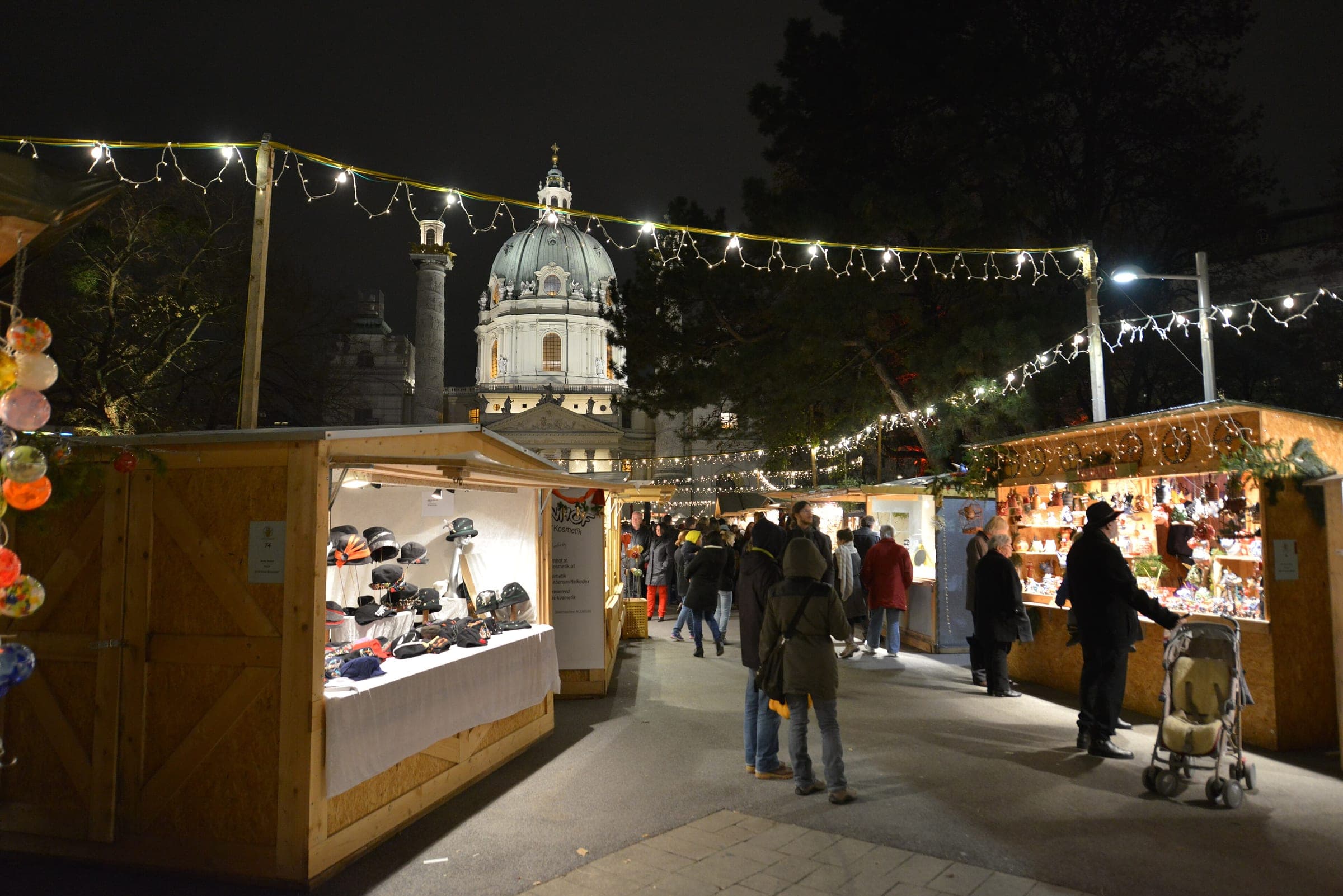 Strings of lights hang over the wooden craft stalls of the Karlsplatz market in Vienna below the Karlskirche dome.