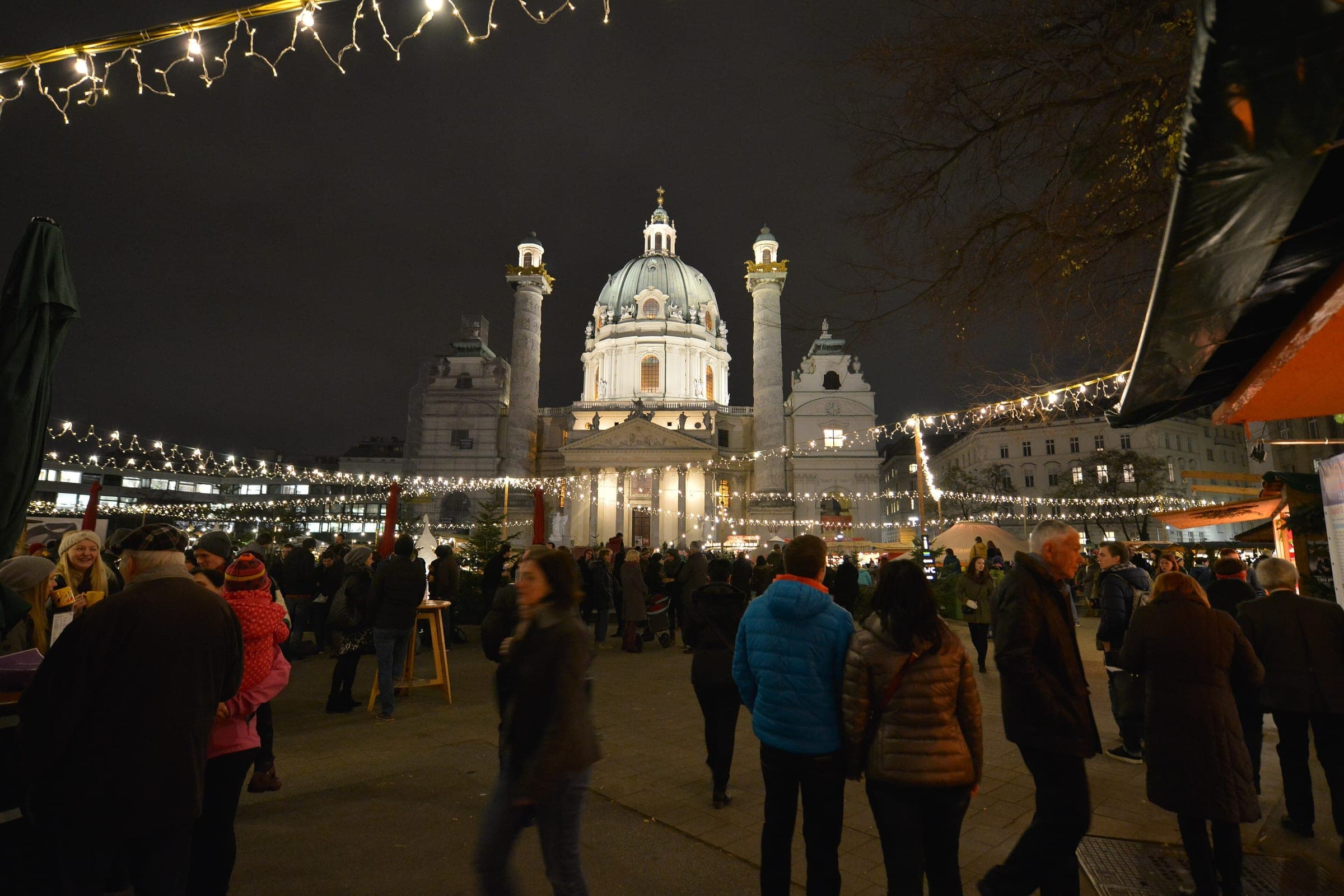 Visitors crowd the Art Advent market on Karlsplatz in Vienna at night below the floodlit Karlskirche.