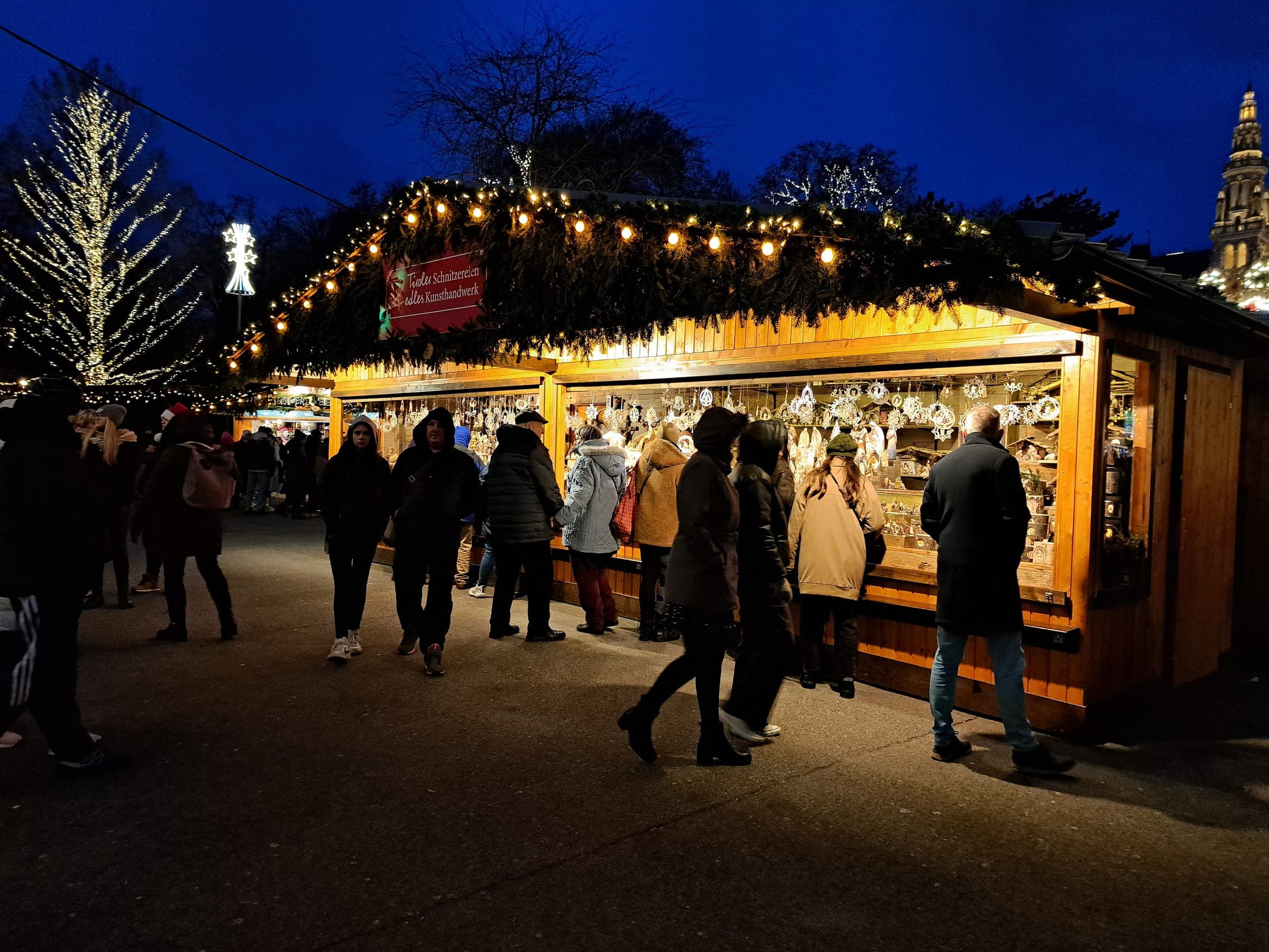 Shoppers gather at a lit wooden stall of the Rathausplatz Christmas market in Vienna after dark.