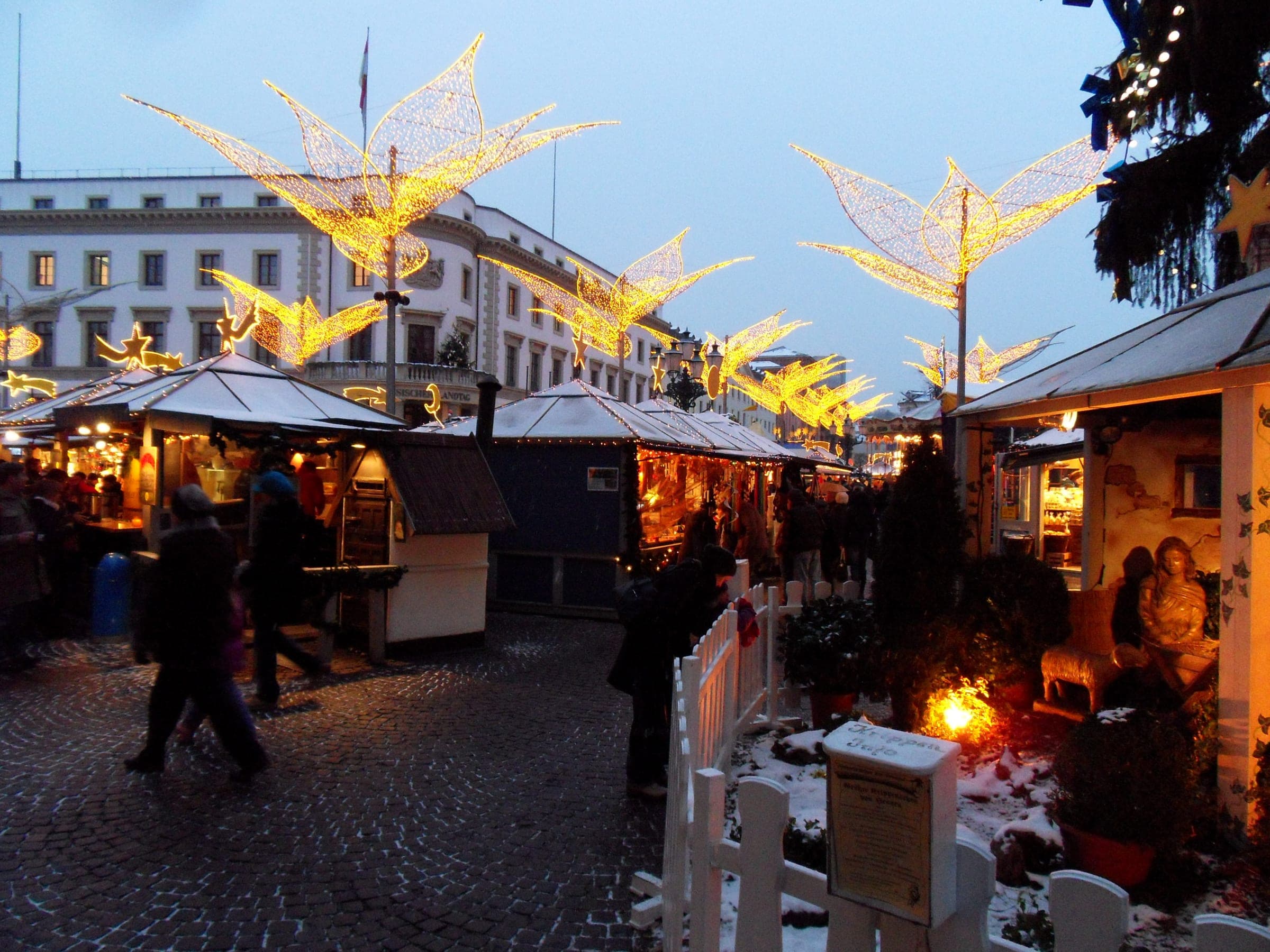 Golden lily lights rise over the stalls of the Sternschnuppenmarkt on Wiesbaden's Schlossplatz at dusk.