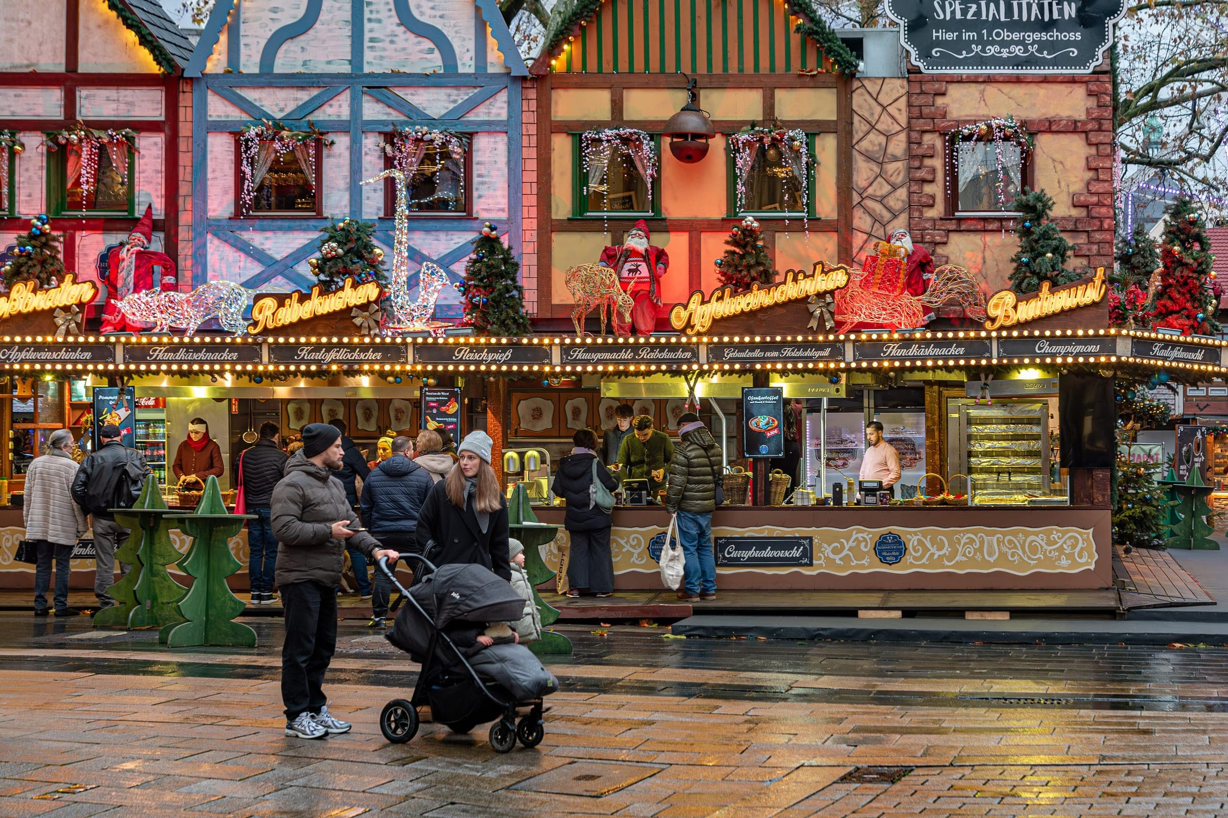 A sweets stall painted like a row of timber-framed houses glows on the wet cobbles of the Wiesbaden market.