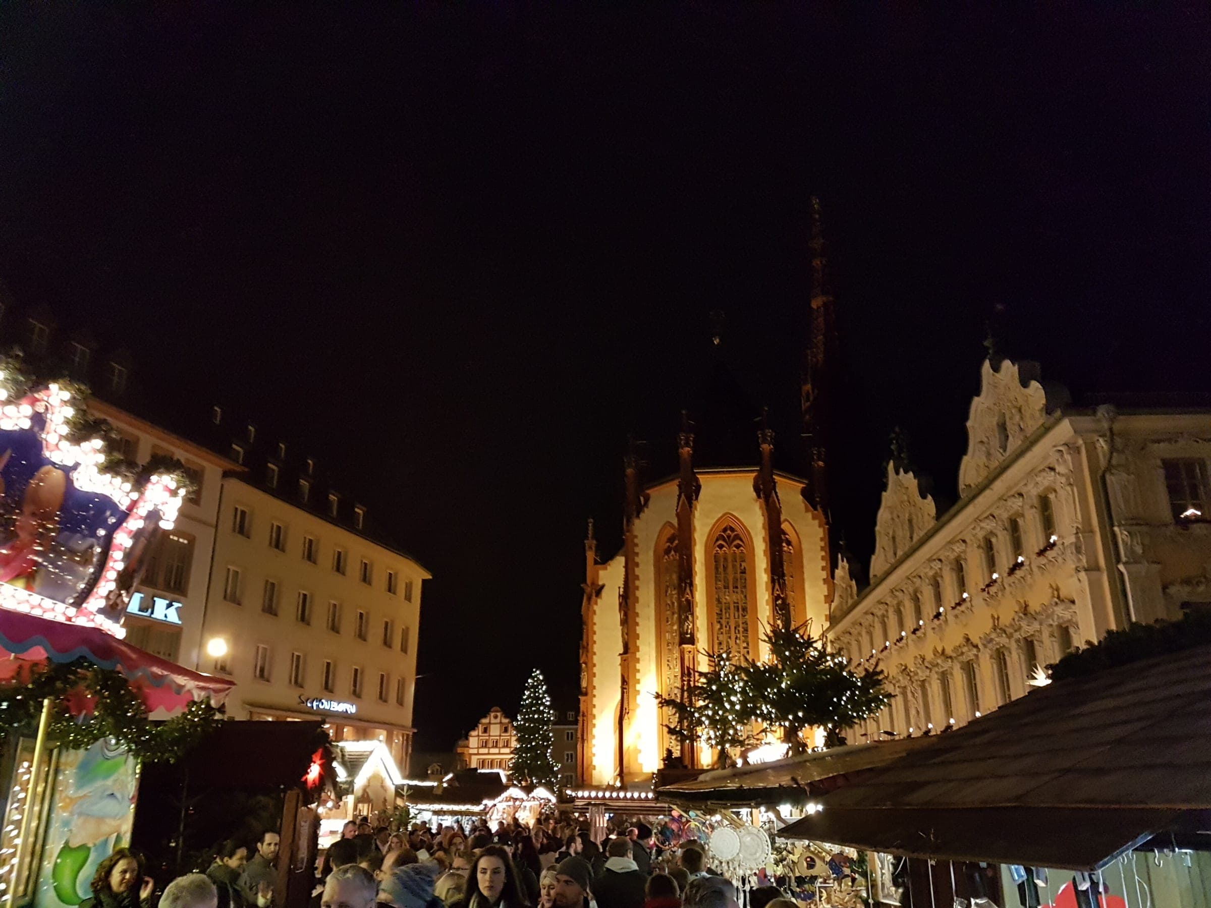 The floodlit Marienkapelle rises above the crowd and stalls of the Würzburg Christmas market at night