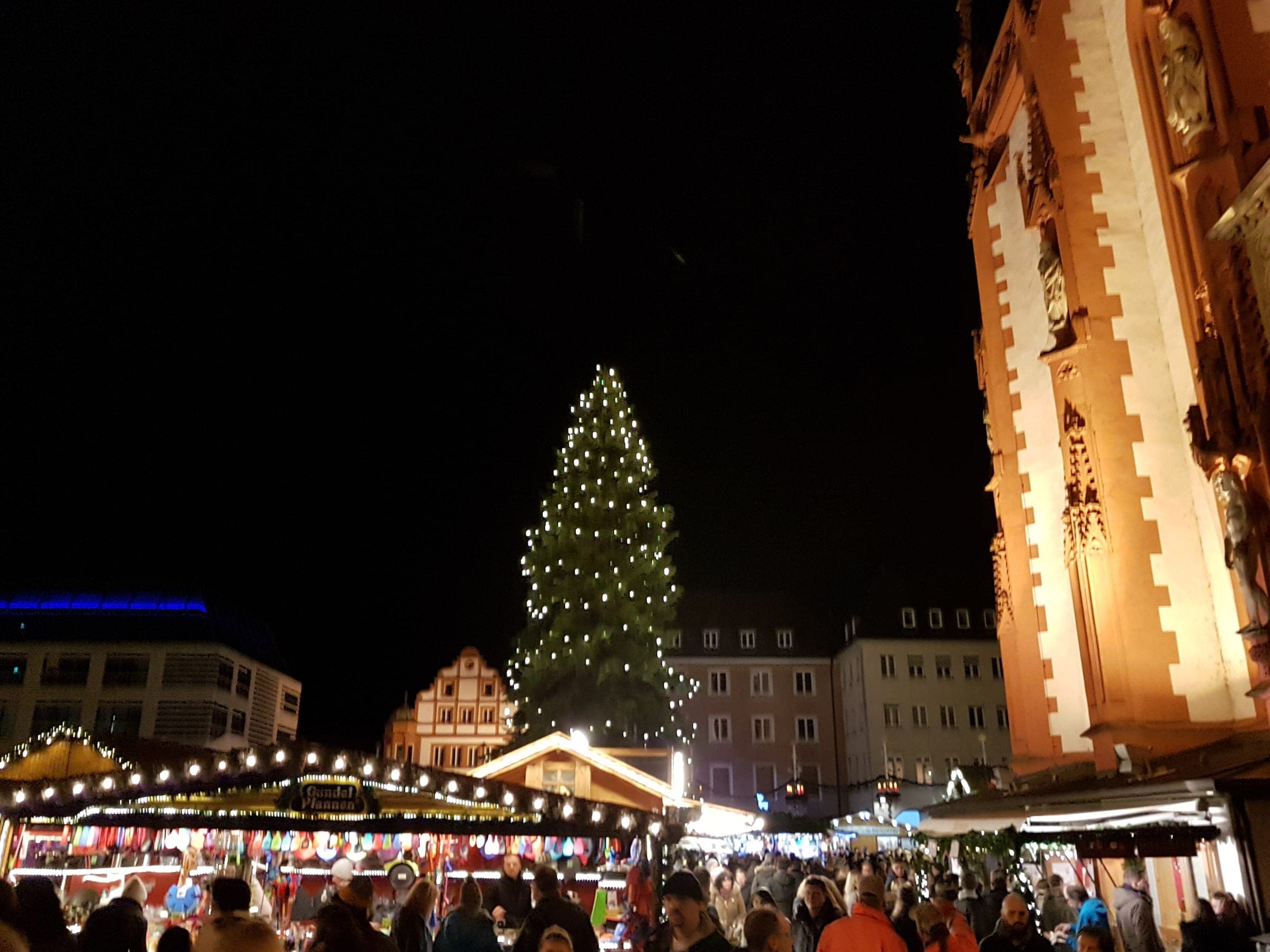 A tall lit tree and the Marienkapelle's red and white facade frame the stalls on Würzburg's Marktplatz at night
