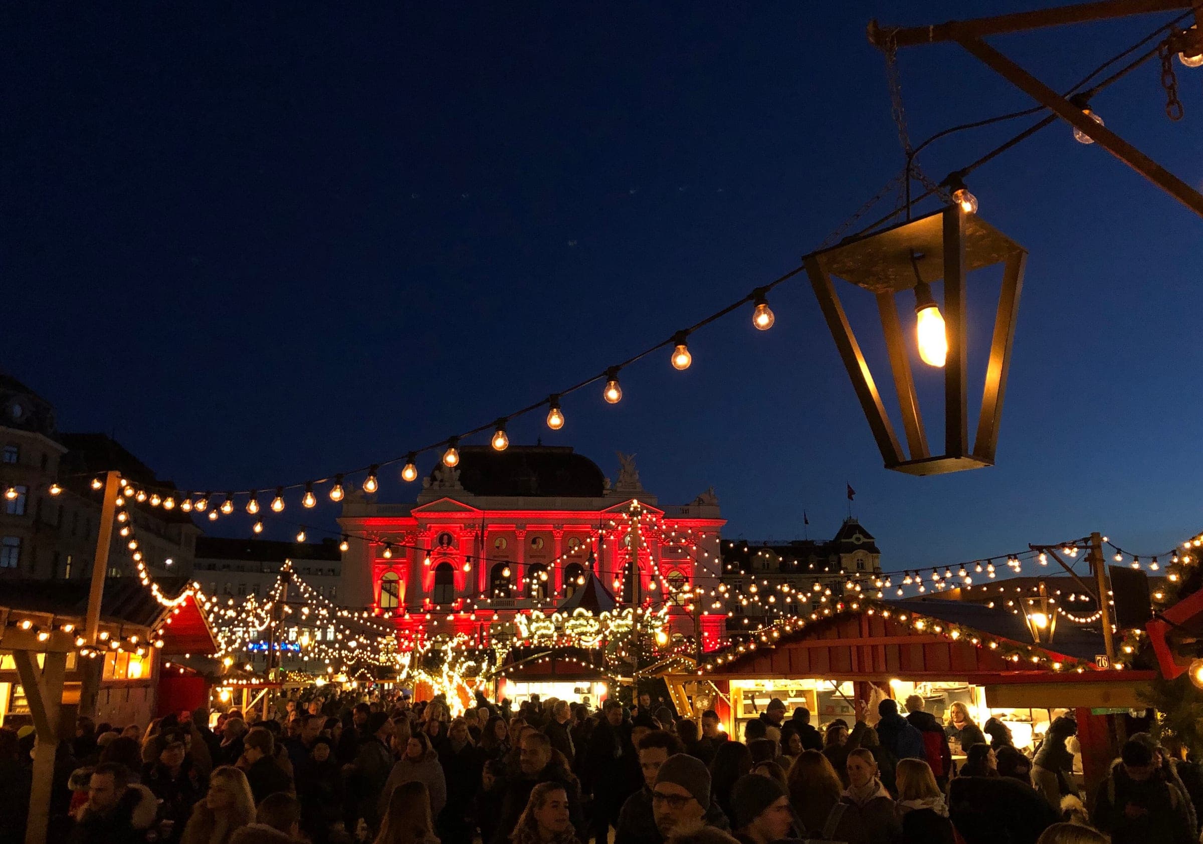 Strings of lights run over the crowded market on Sechseläutenplatz in Zurich toward the red-lit opera house