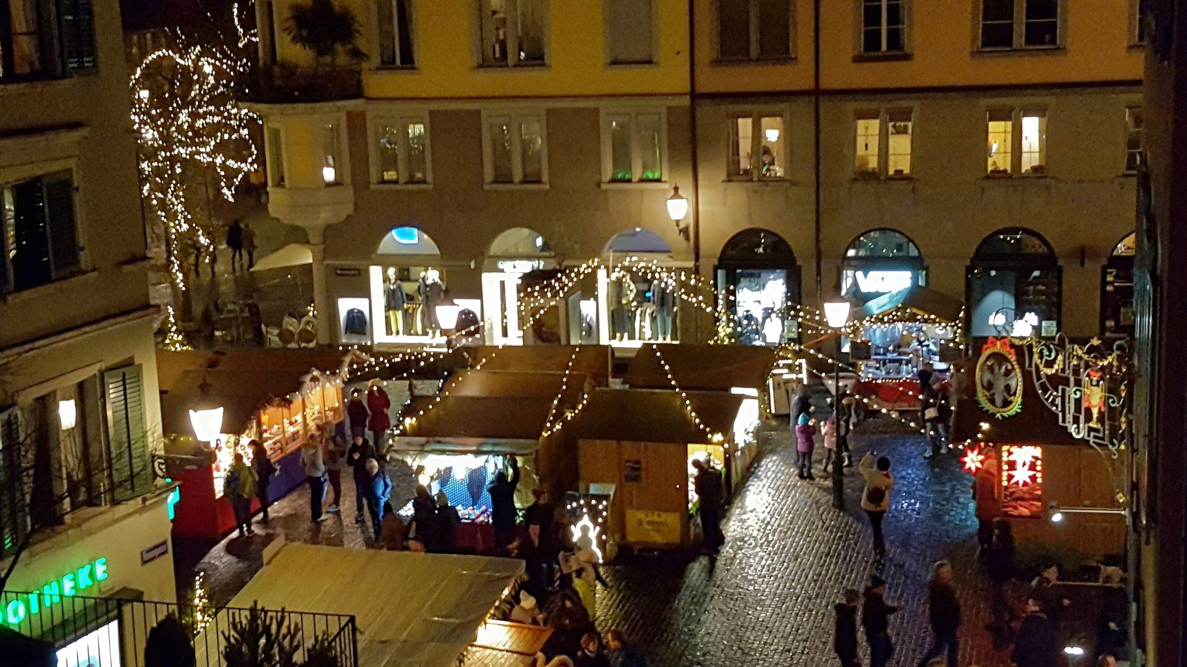 Lit wooden huts of the Dörfli Christmas market crowd Hirschenplatz in Zurich's Niederdorf at night