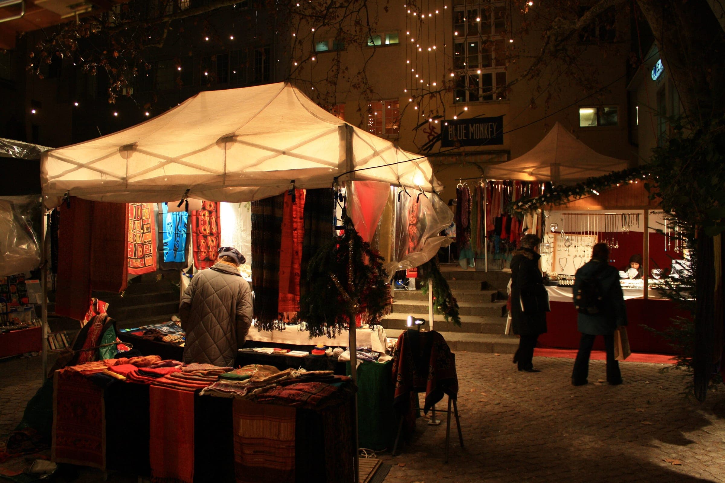 Shoppers browse lit market tents under strings of lights in the Rosenhof in Zurich at night