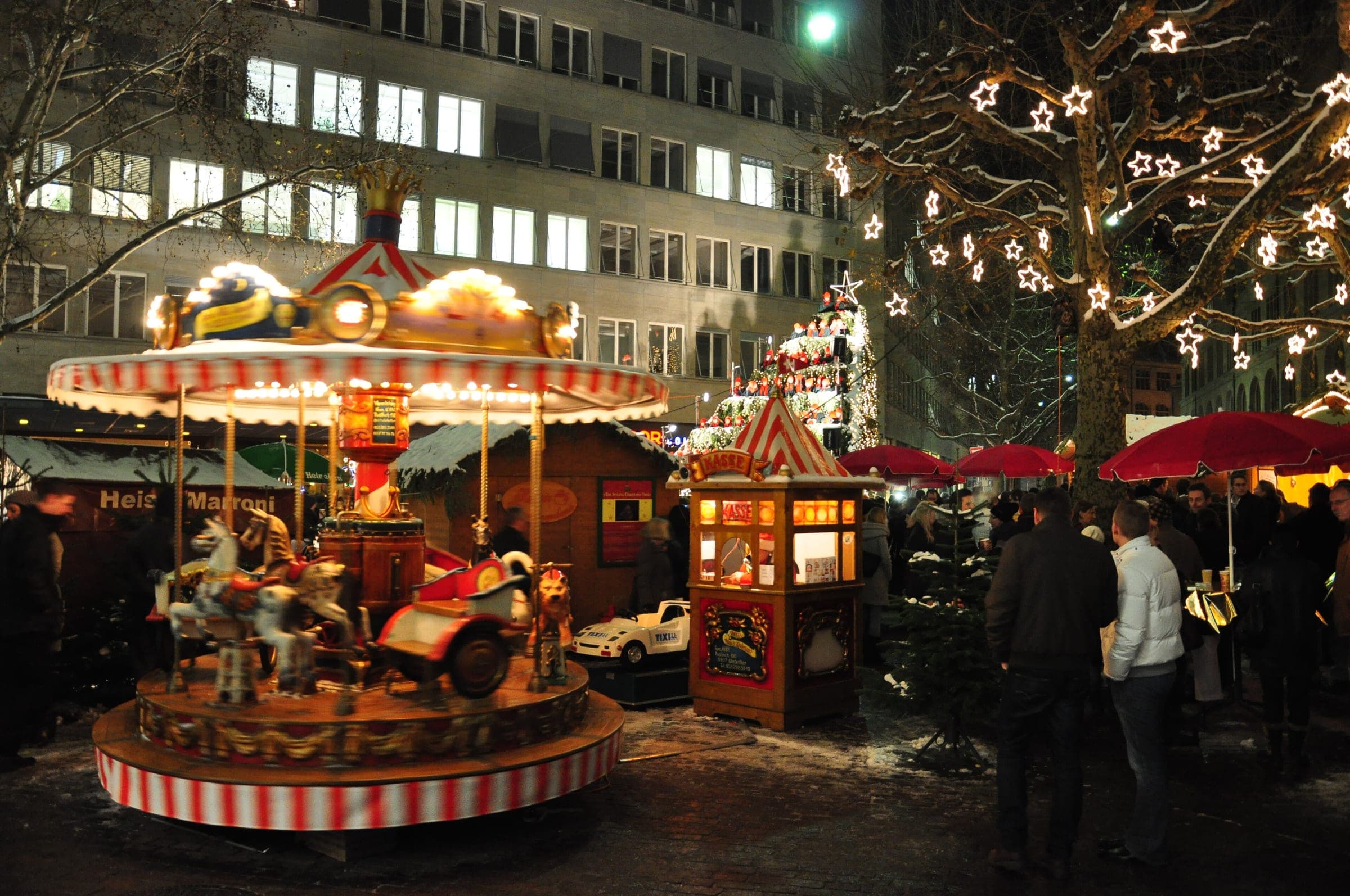 A lit carousel turns beside the market stalls on Werdmühleplatz in Zurich on a December evening