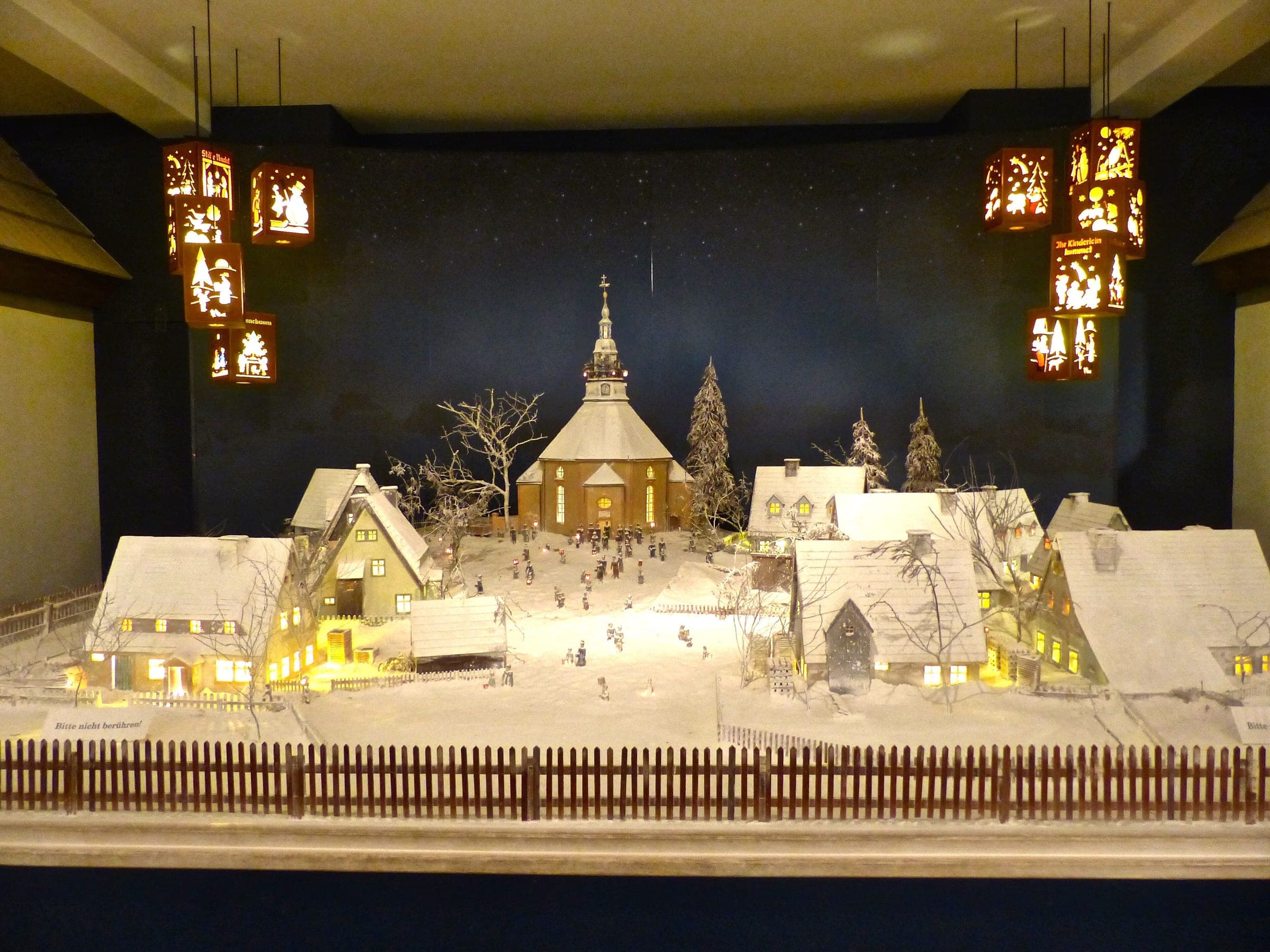 Lit paper lanterns hang over a snowy model of Seiffen and its church in the Erzgebirge Toy Museum.