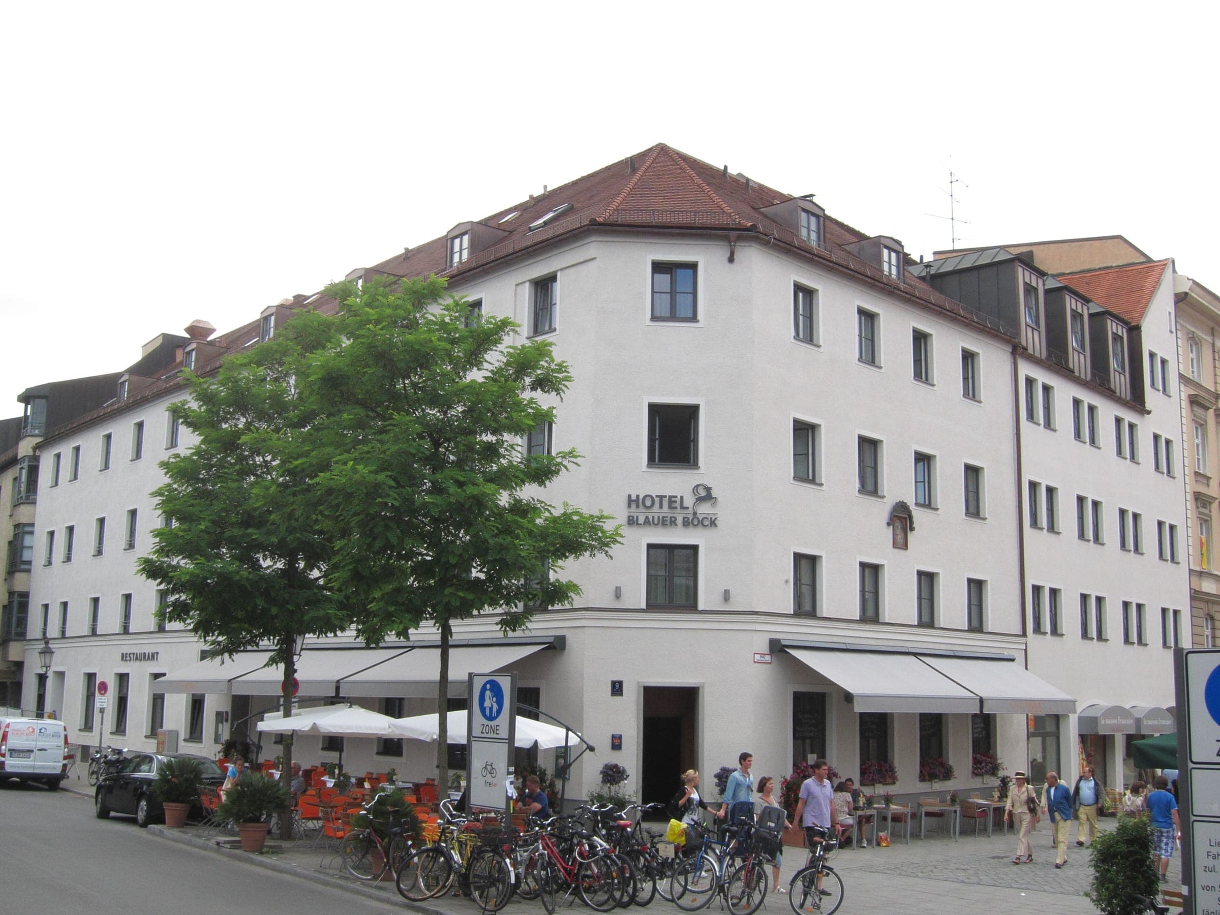 Café tables and bikes fill the pavement below Hotel Blauer Bock's white corner on Sebastiansplatz in Munich.