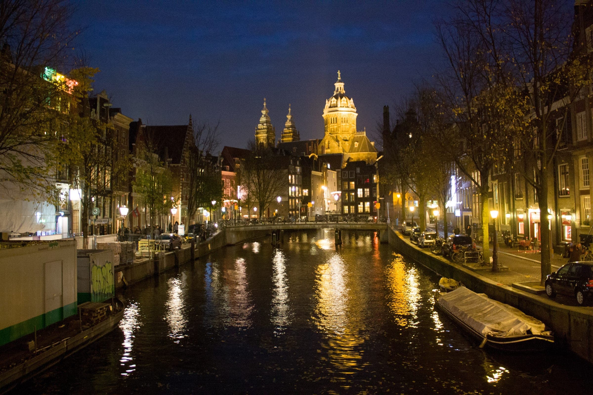 Street lamps shine on the Oudezijds Voorburgwal in Amsterdam at night below the domes of Sint-Nicolaaskerk.