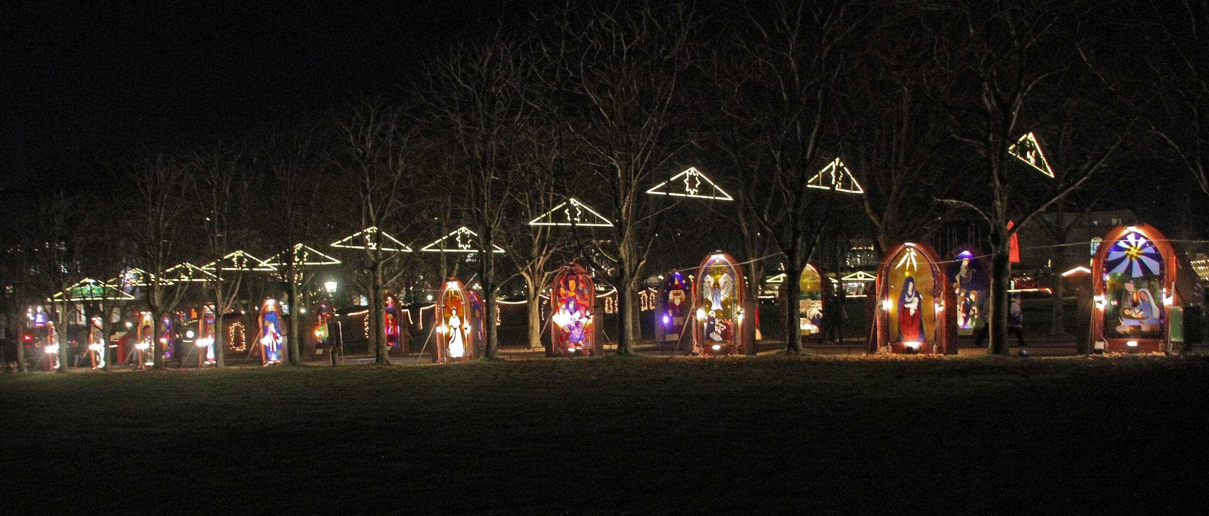 A row of backlit pictures and star frames glows along the Kurgarten paths at the Baden-Baden market at night.