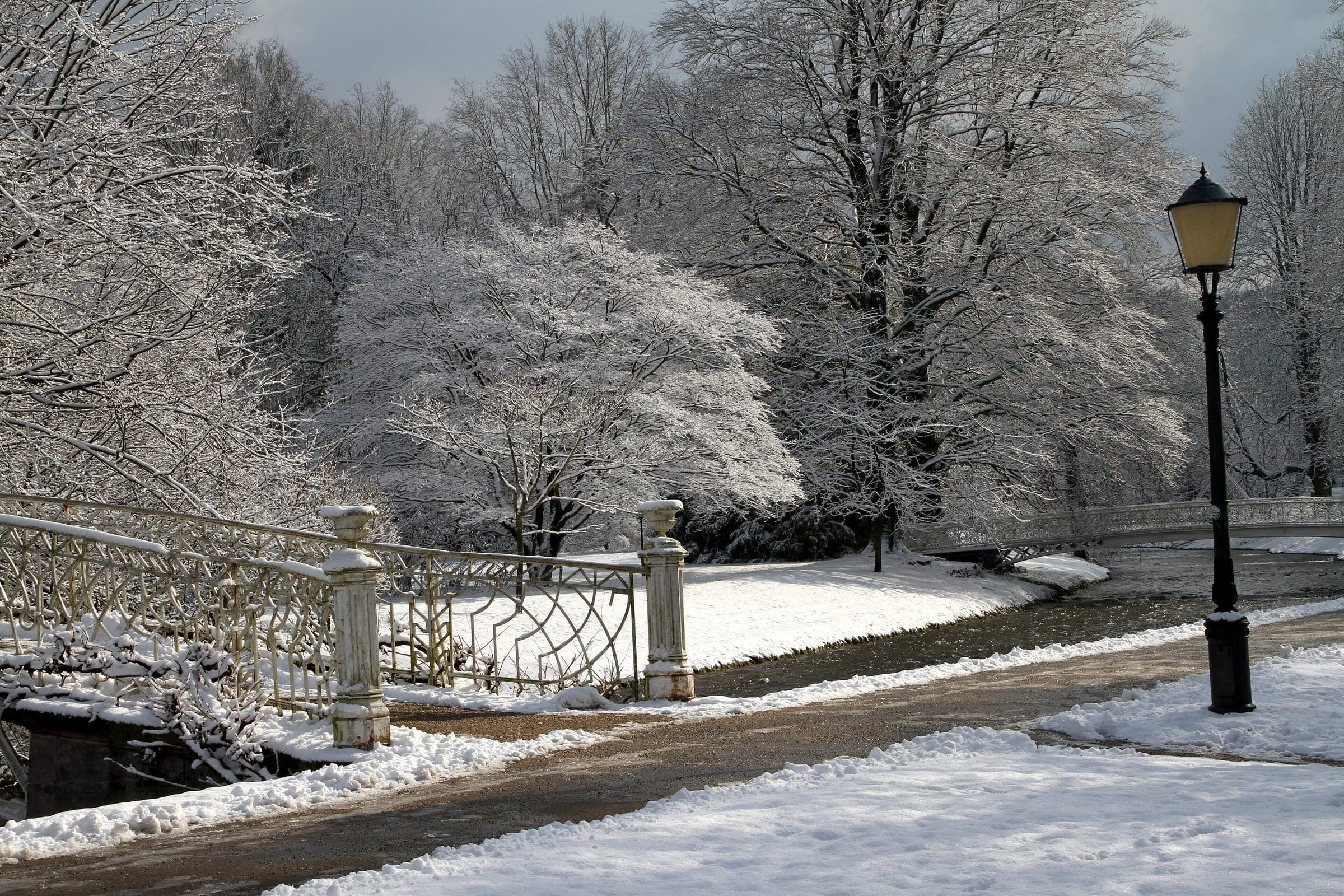 A wrought-iron bridge crosses the Oos between frosted trees in Baden-Baden's spa park.