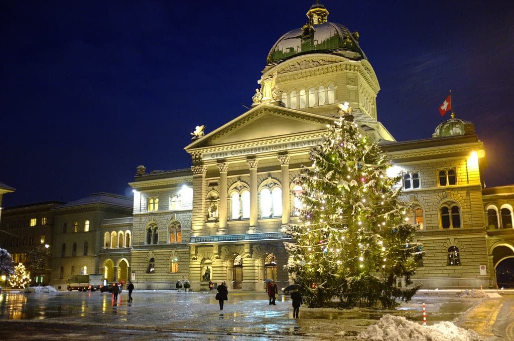 A lit Christmas tree stands on Bundesplatz in Bern before the Federal Palace on a snowy night