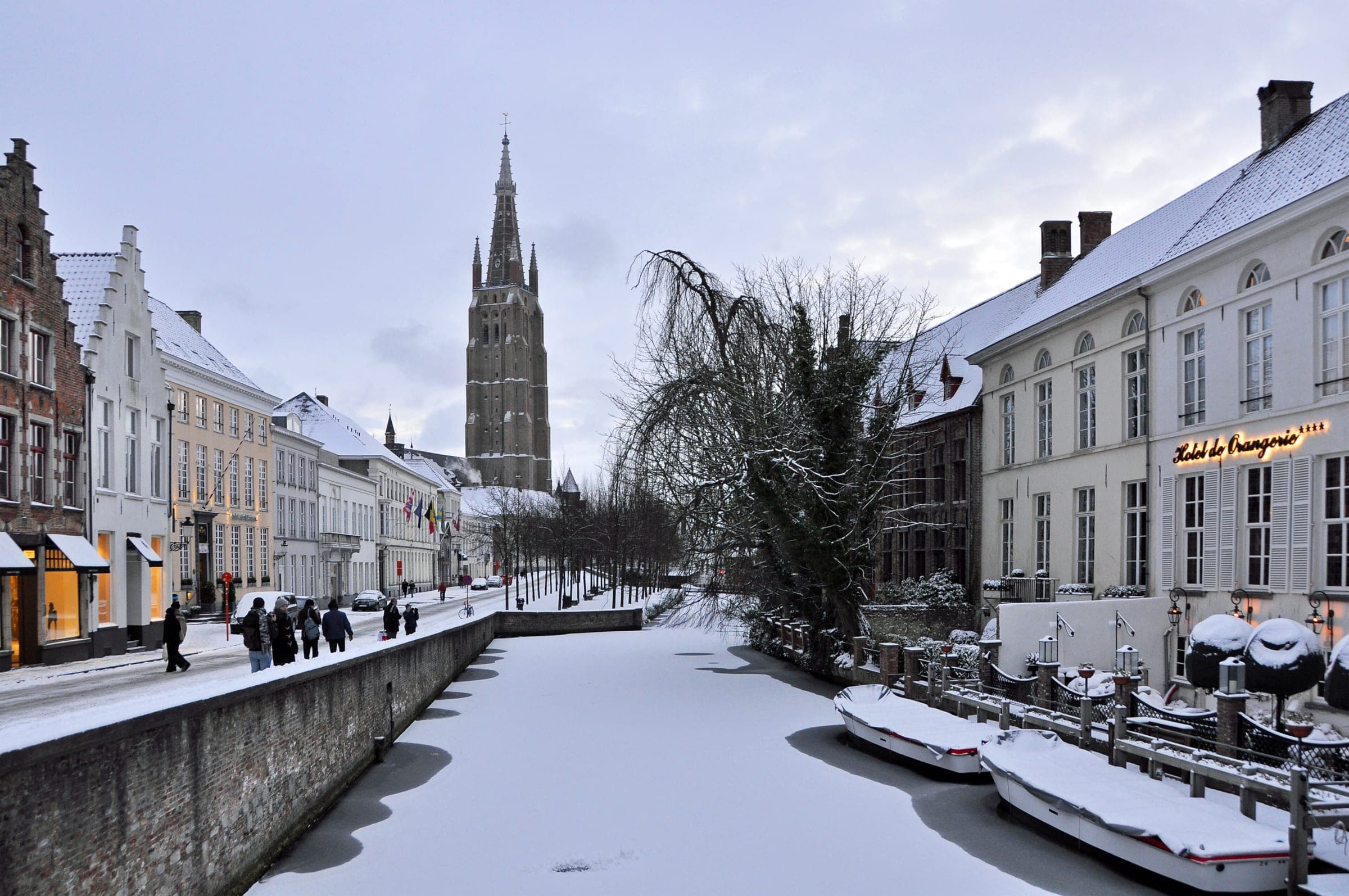Snow covers the Dijver in Bruges, where the frozen canal leads toward the spire of the Church of Our Lady.