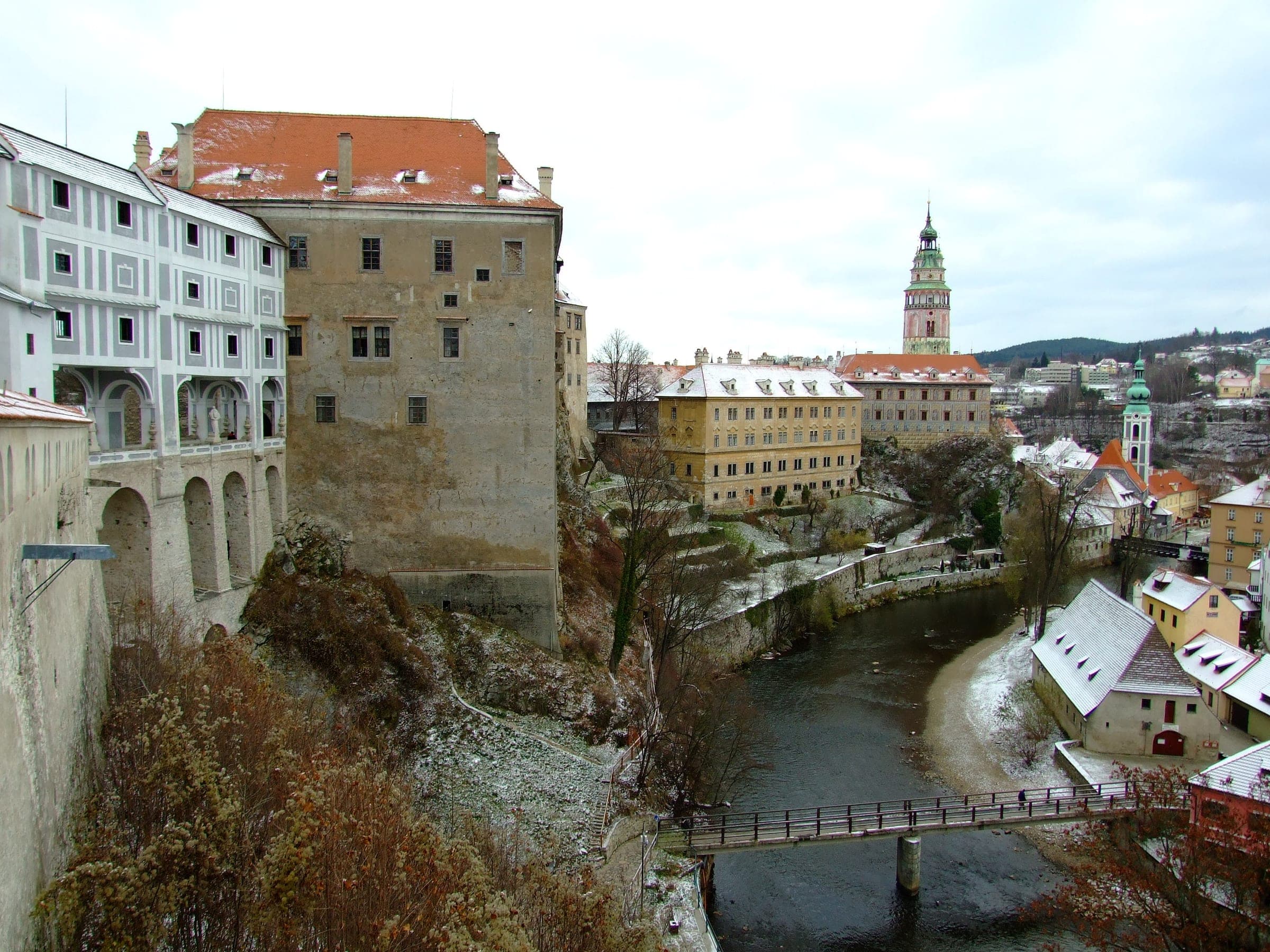 Snow dusts the castle walls and the painted tower of Český Krumlov above the Vltava footbridge.