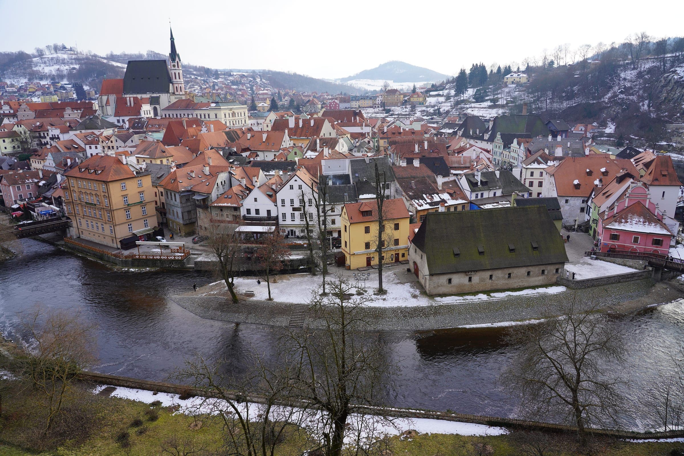 The Vltava curls past snowy rooftops in Český Krumlov below the spire of St Vitus Church.