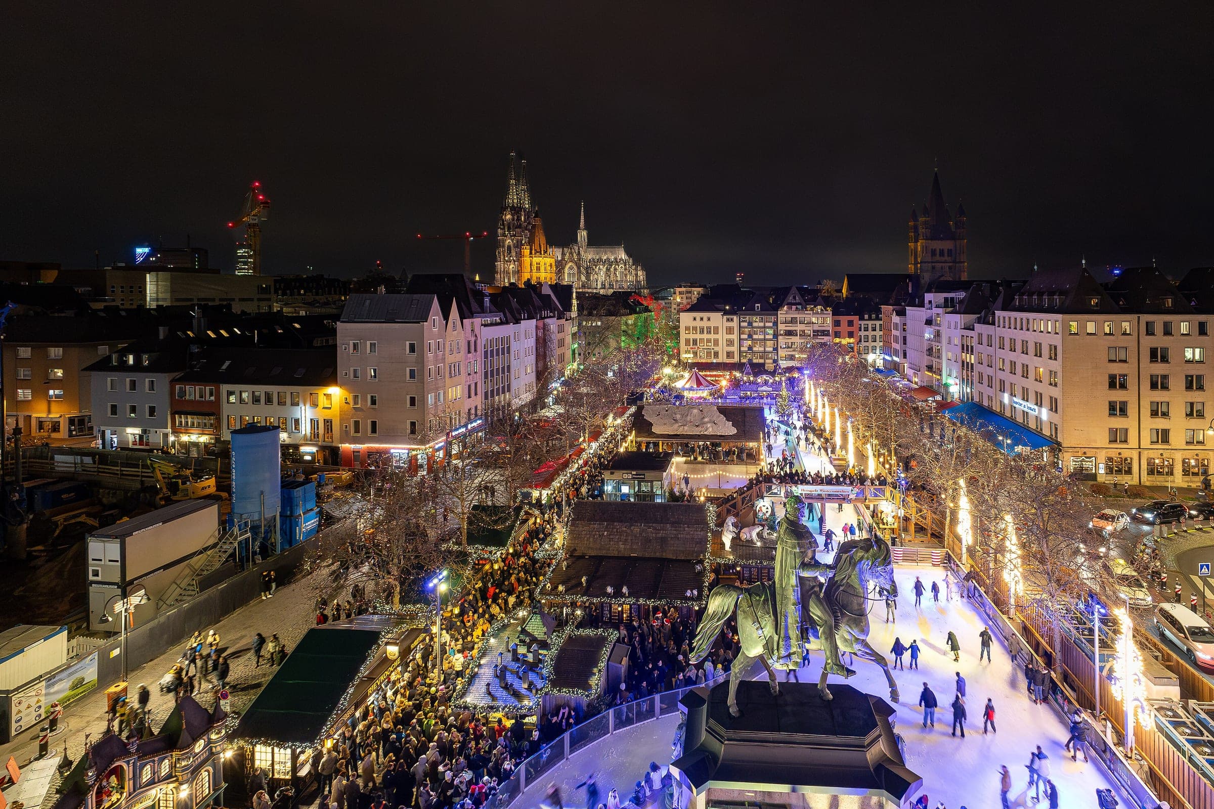 The Heumarkt Christmas market and ice rink glow around a bronze rider with Cologne Cathedral behind