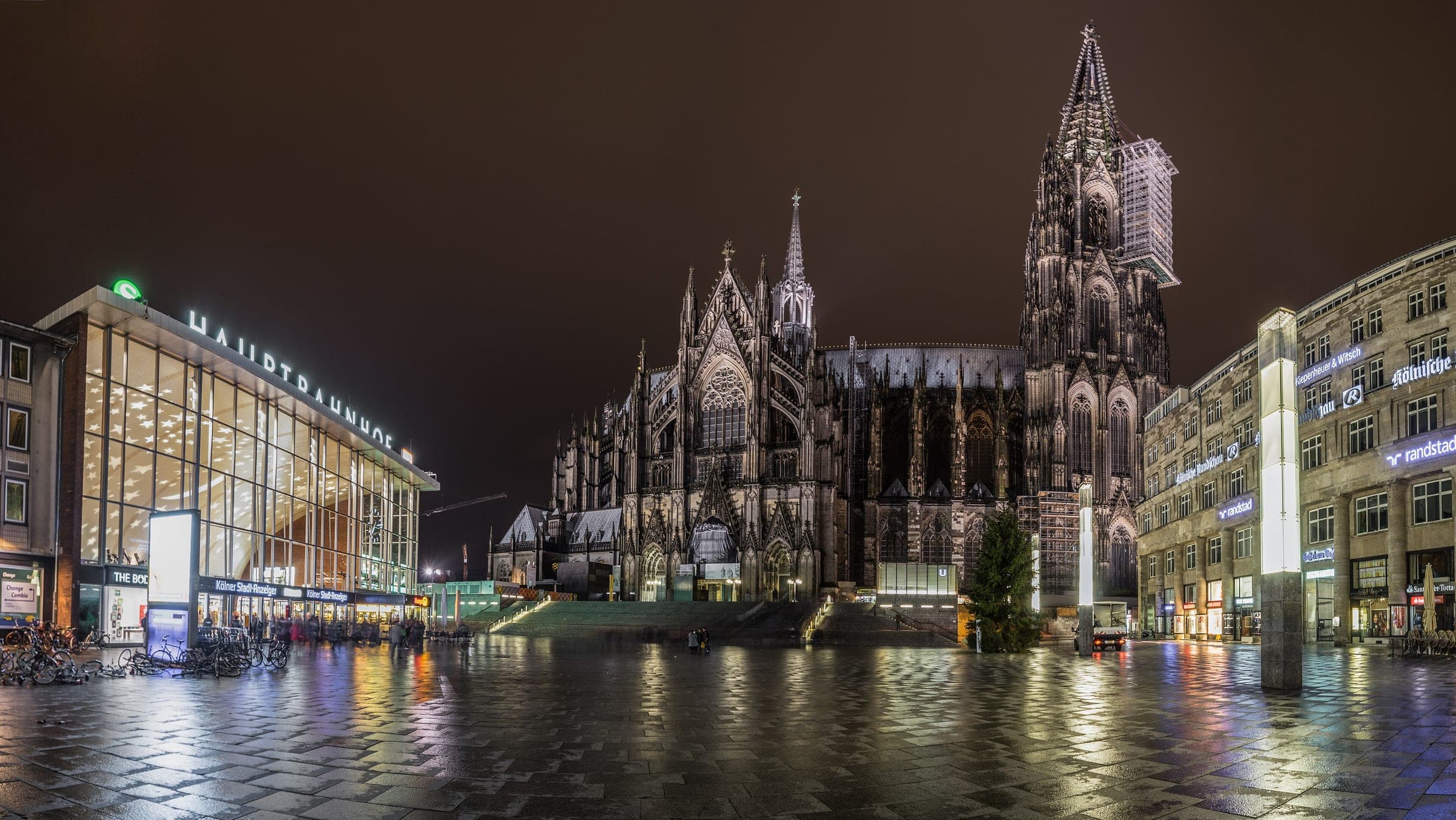 Cologne Cathedral and the main station face each other across a wet, lit square at night