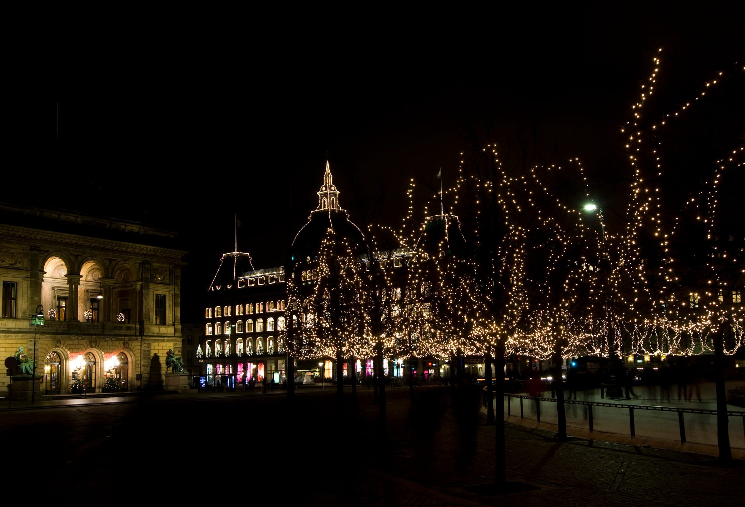 Bare trees wound with white lights ring Kongens Nytorv in Copenhagen on a December night by the Royal Theatre.