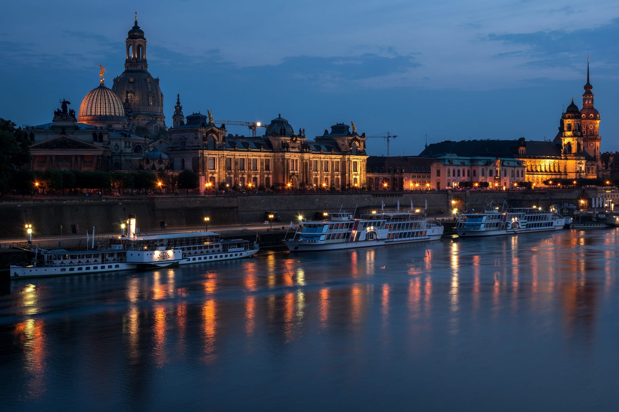 Dresden's old town skyline with the Frauenkirche dome glows over the Elbe at blue hour.