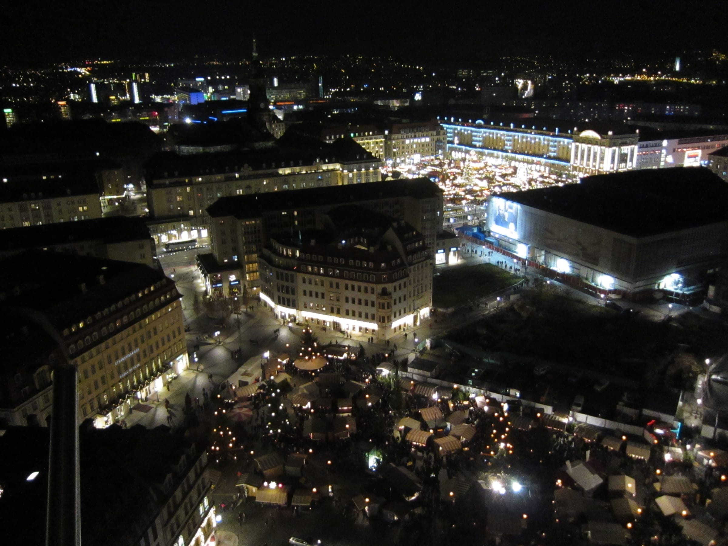 The lit Striezelmarkt glows on the Altmarkt in this night view over Dresden from the Frauenkirche dome.