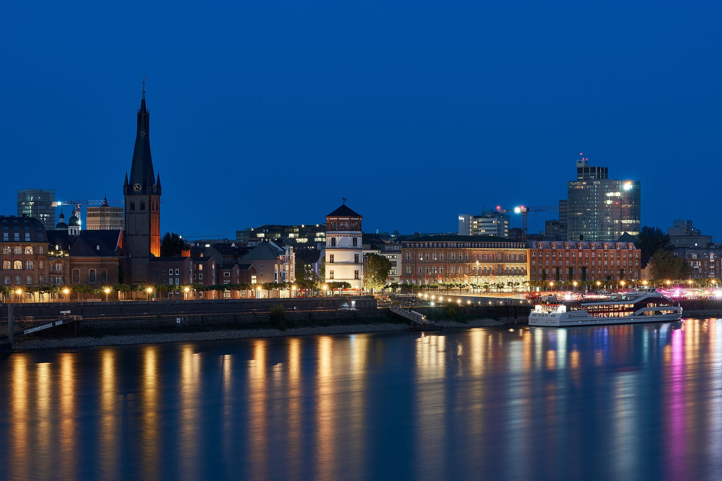 St Lambertus and the Schlossturm light up the Düsseldorf Altstadt riverfront on the Rhine at blue hour