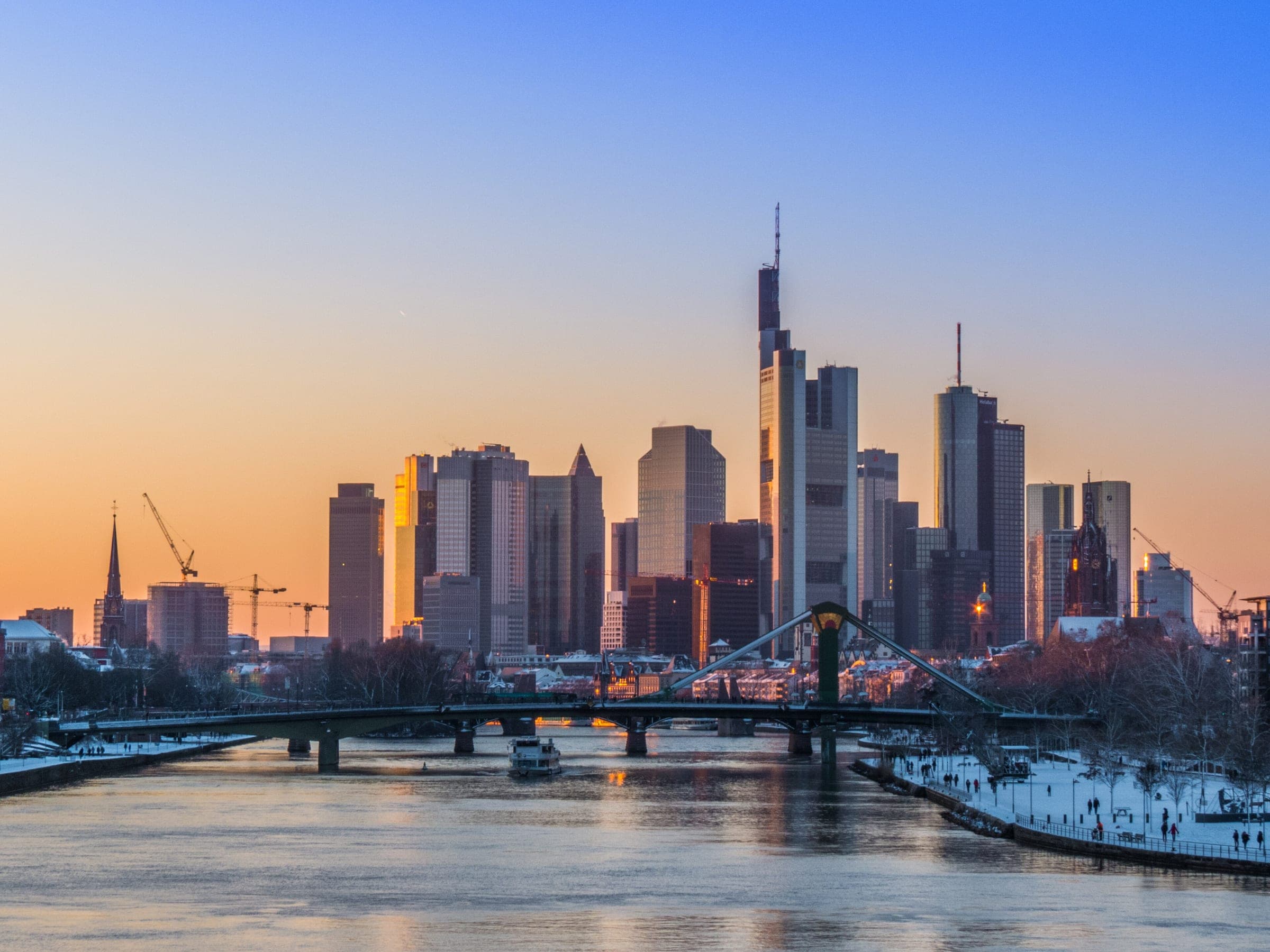 Frankfurt's towers glow at sunset above the Main as snow lines the riverbank.