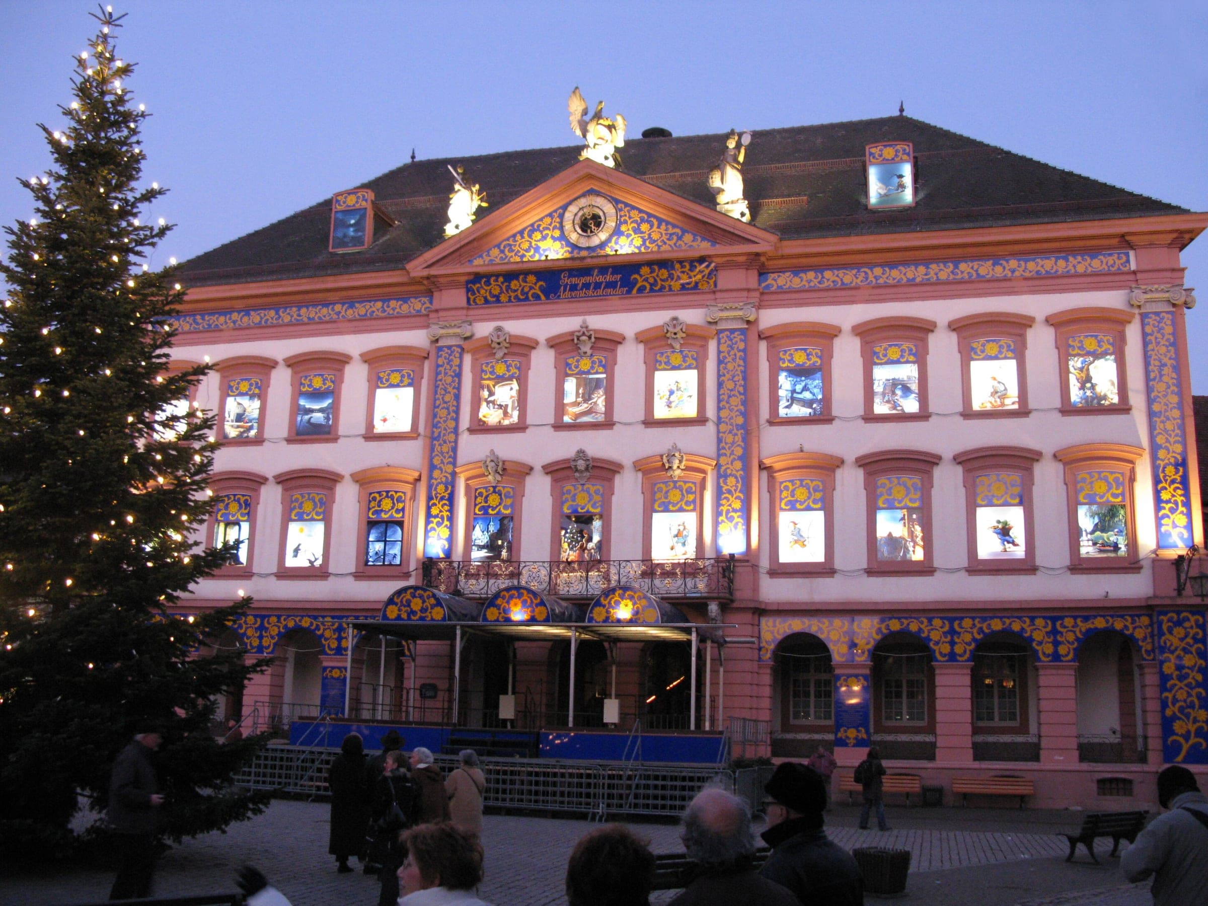 Gengenbach's Rathaus stands lit as an Advent calendar house beside a tall Christmas tree at dusk.