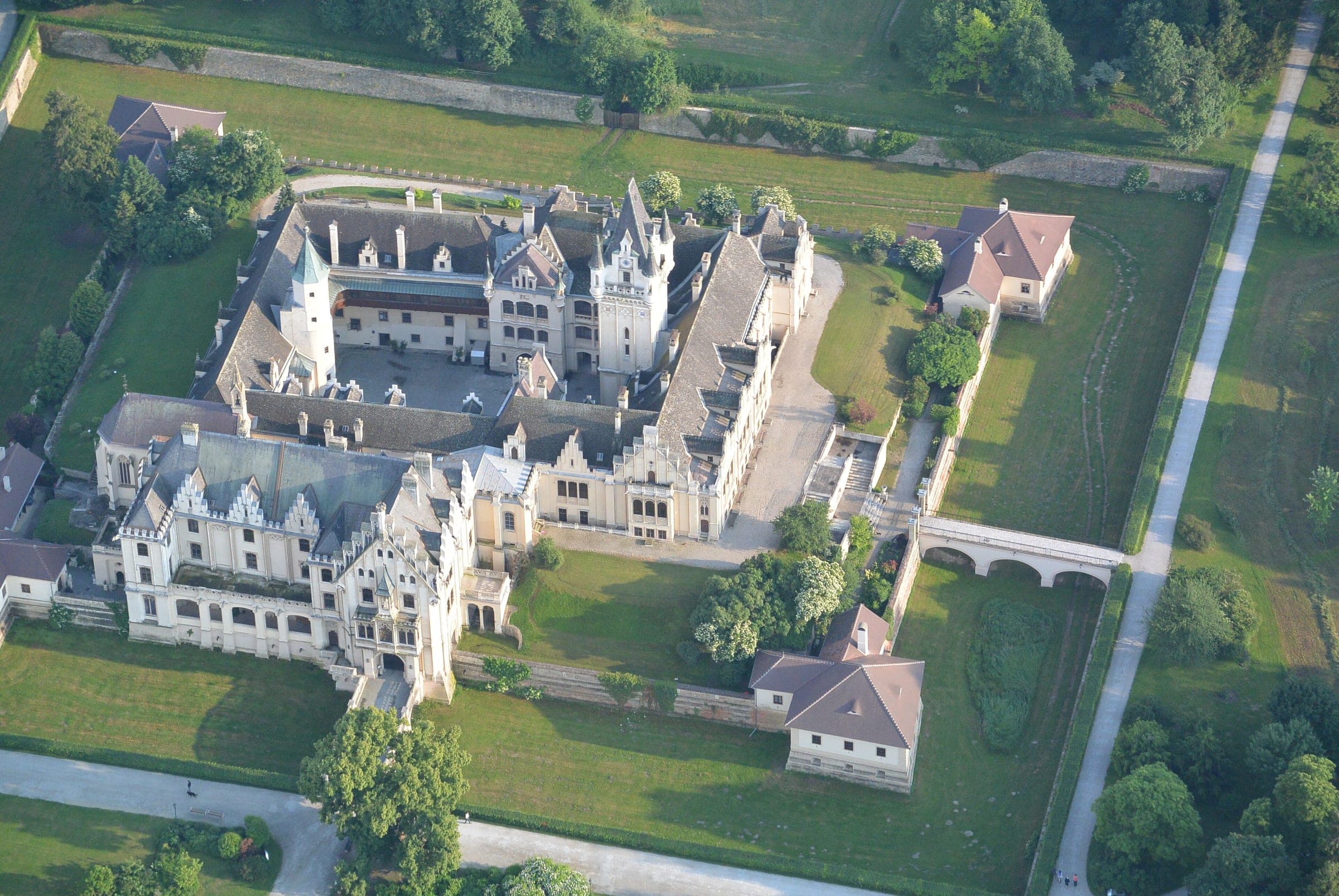 An aerial view shows Schloss Grafenegg and its courtyards set among lawns and park trees.