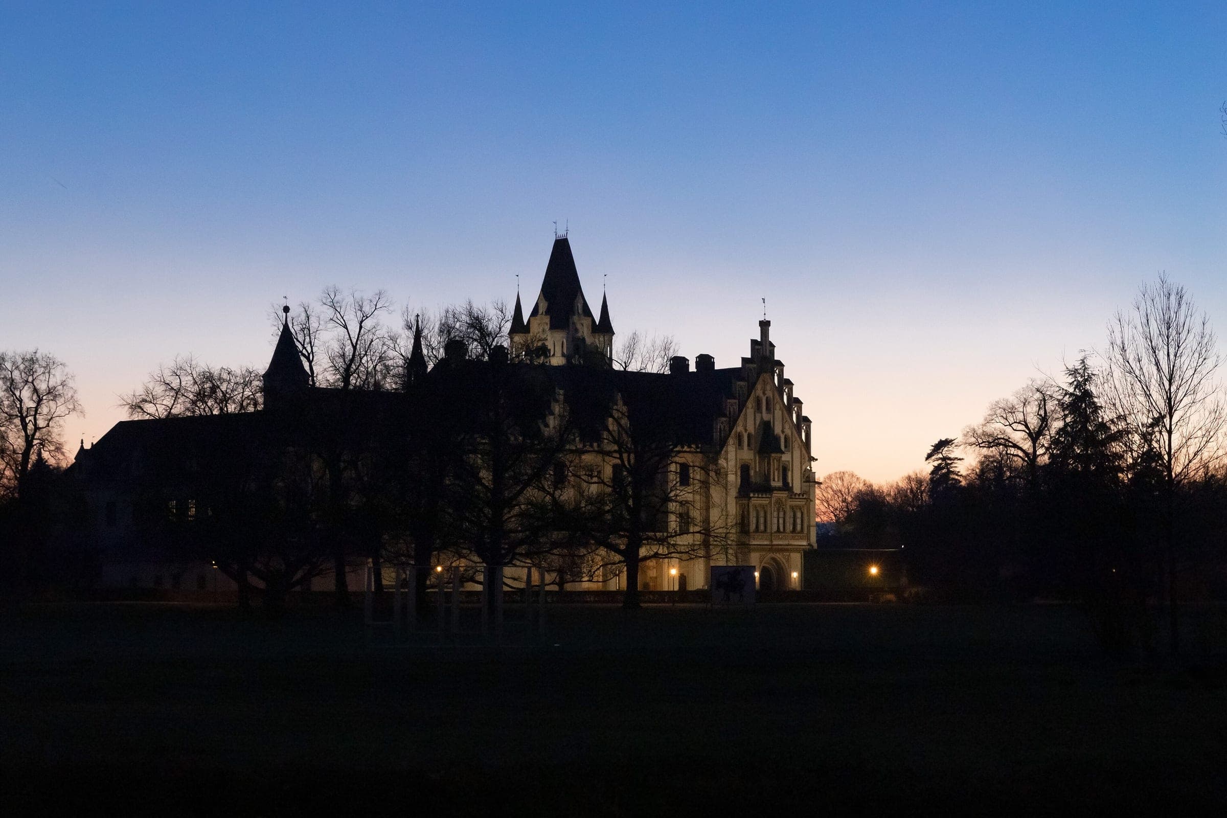 Schloss Grafenegg stands in silhouette behind bare winter trees as the sky fades after sunset.