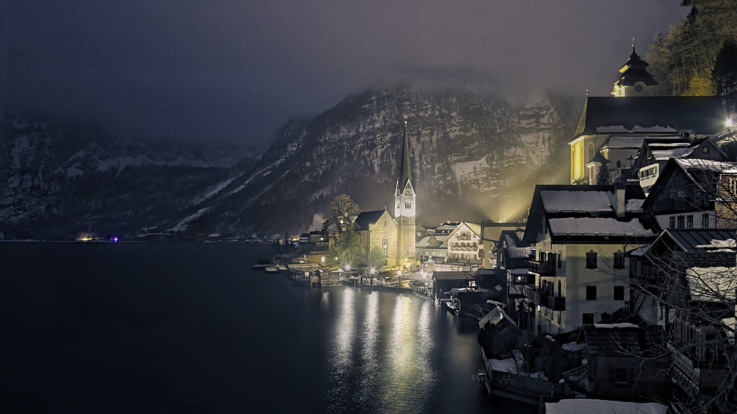 Hallstatt's church and lakeside houses glow at night under snowy mountains on the Hallstätter See