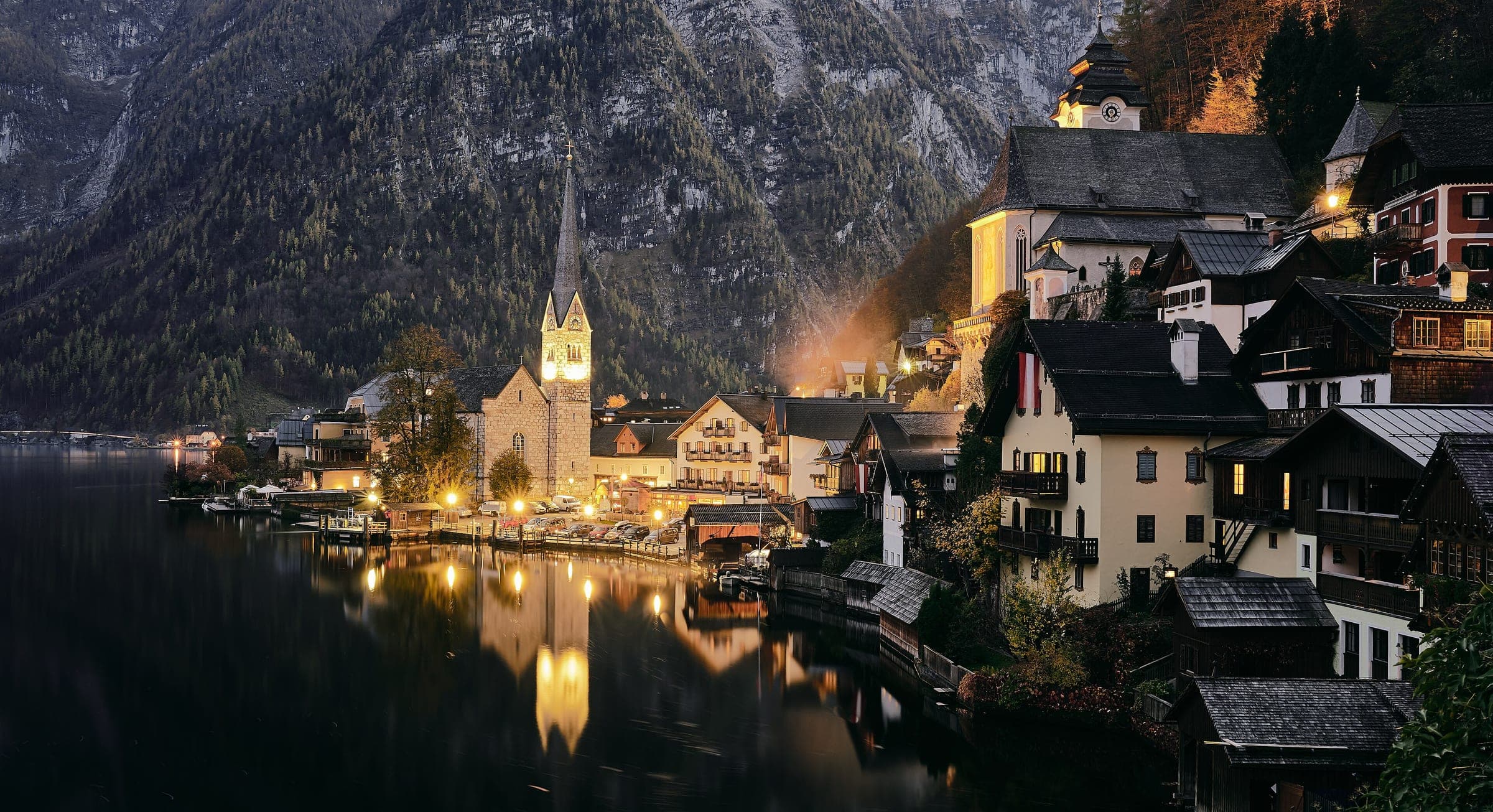 Lights come on along the lakeside houses and church spire of Hallstatt in the late evening
