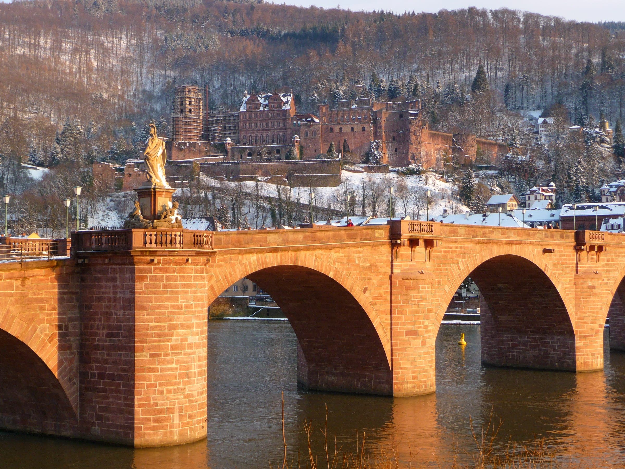 Evening sun warms the Old Bridge in Heidelberg as snow lies on the castle hill behind it.