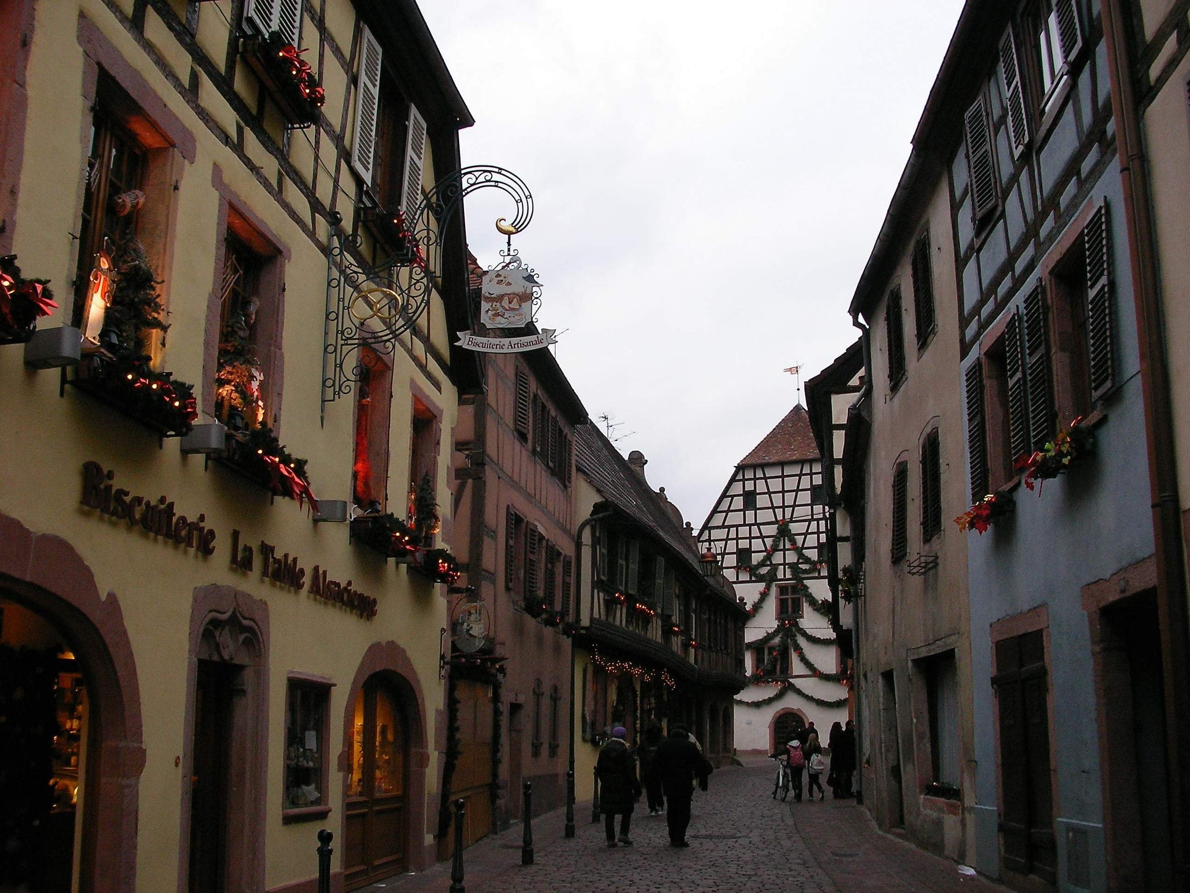 Garlands and lit windows decorate the Grand'Rue of Kaysersberg on a grey December afternoon.