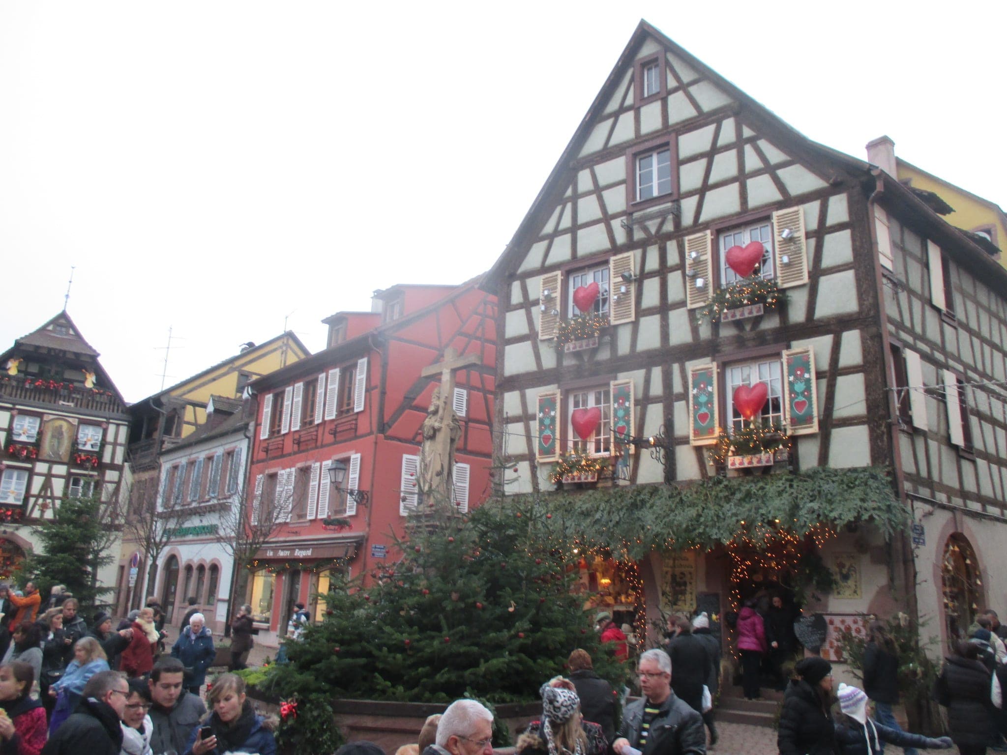Red hearts hang in the windows of a half-timbered house on a busy square in Kaysersberg in December.
