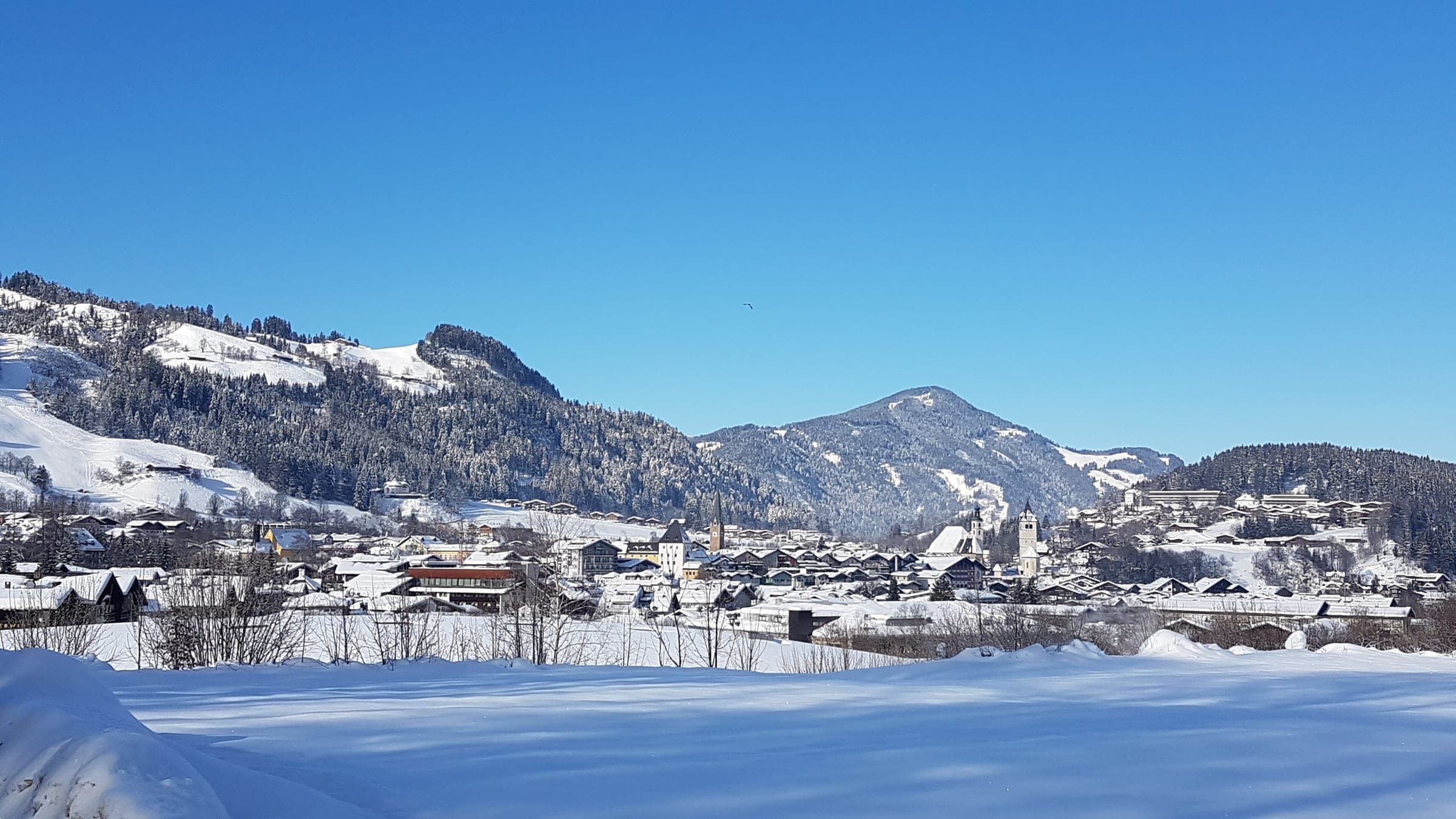 Kitzbühel's church towers and roofs sit in deep snow below the Hahnenkamm slopes on a bright January day.