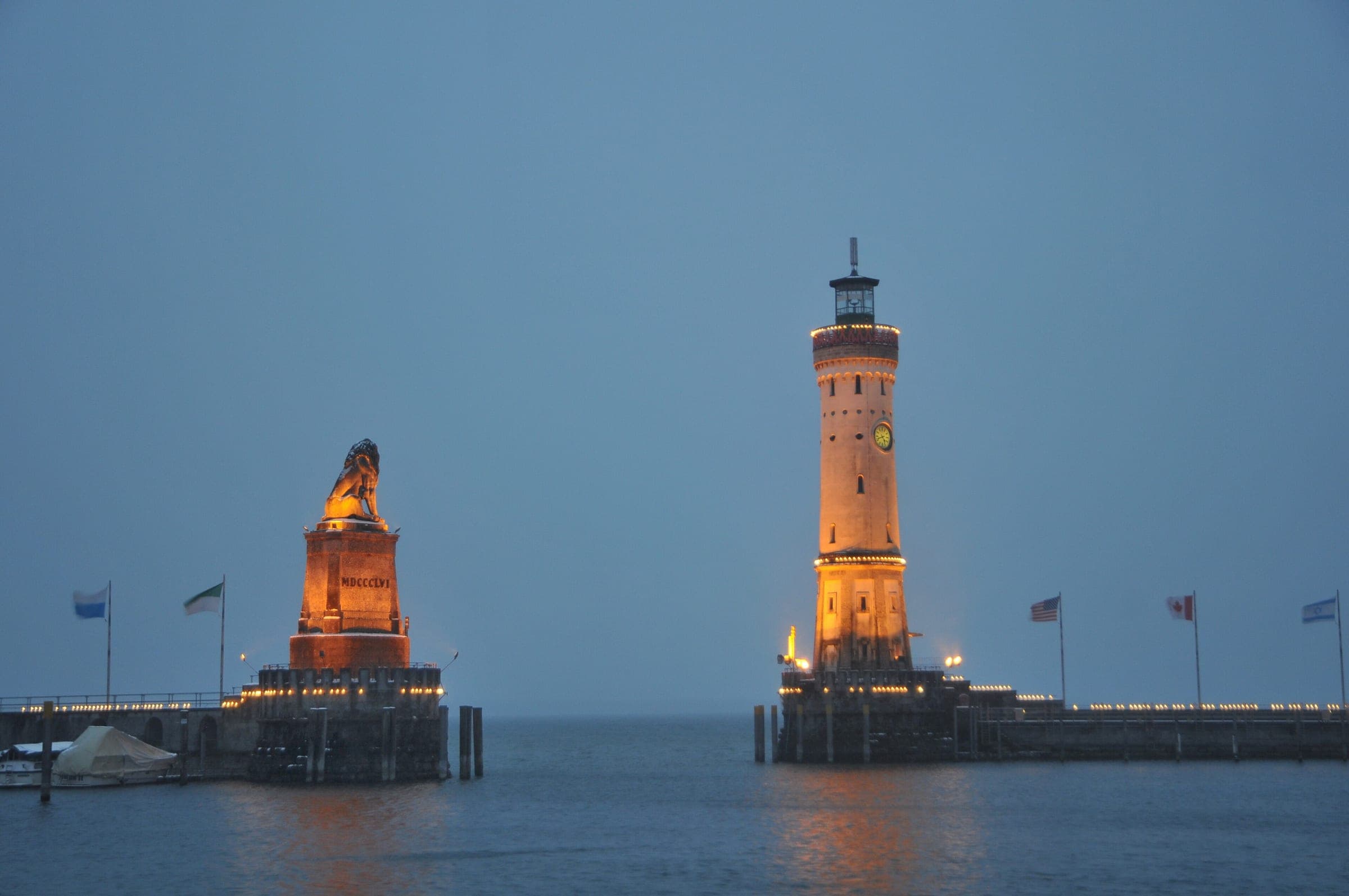 The Bavarian Lion and the lighthouse stand floodlit at the Lindau harbour entrance on a December evening.
