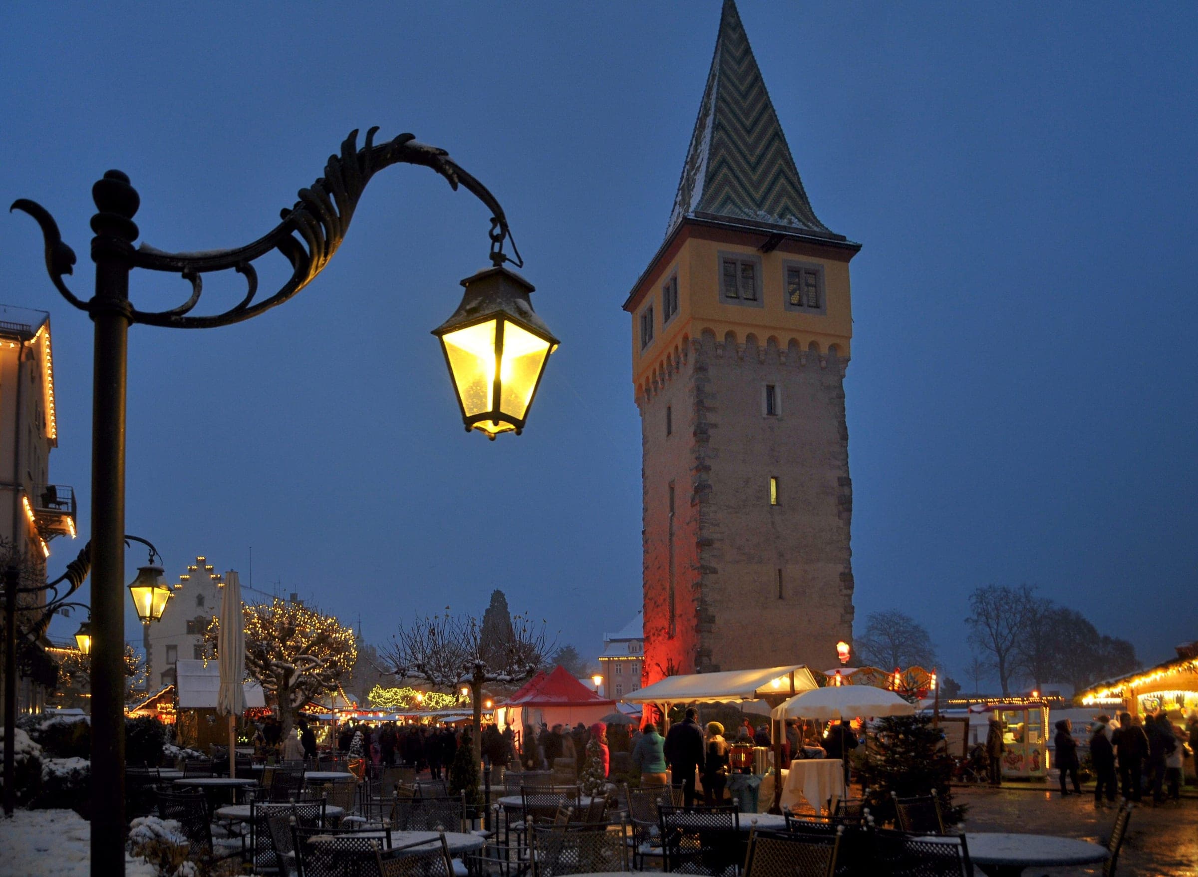 A street lantern glows beside the Mangturm on the Lindau waterfront at blue hour in December.