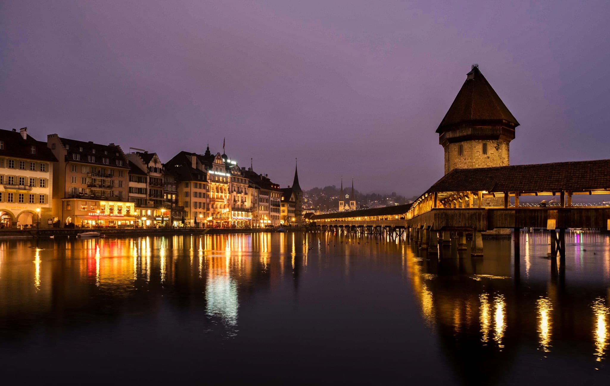Lucerne's old town and the Chapel Bridge glow in the Reuss at dusk under a violet sky