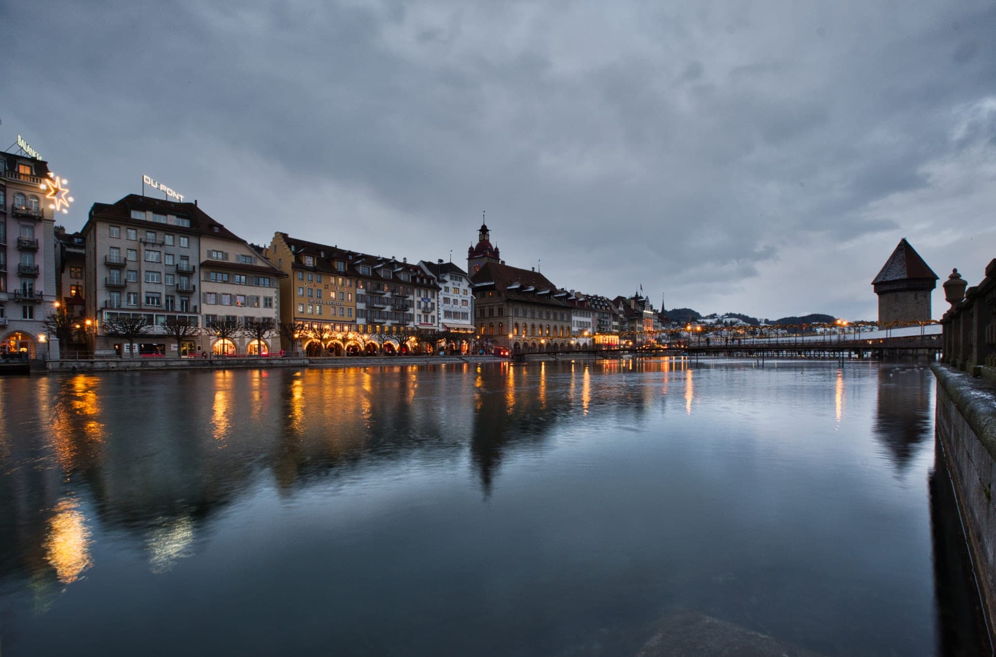 Christmas lights hang along the riverfront houses of Lucerne as they reflect in the still Reuss at dusk