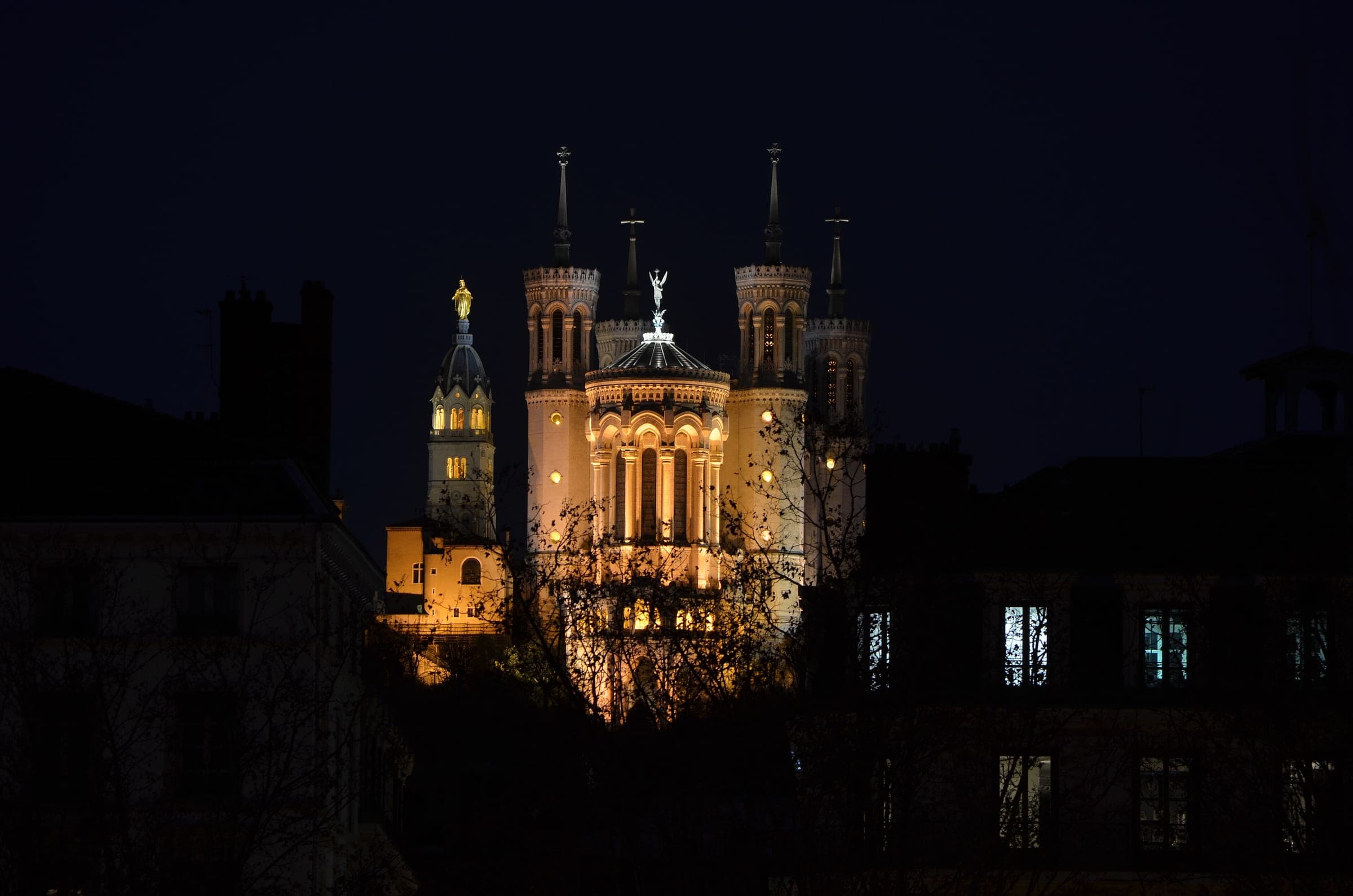 The lit towers of Fourvière basilica rise above dark Lyon rooftops on a December night.