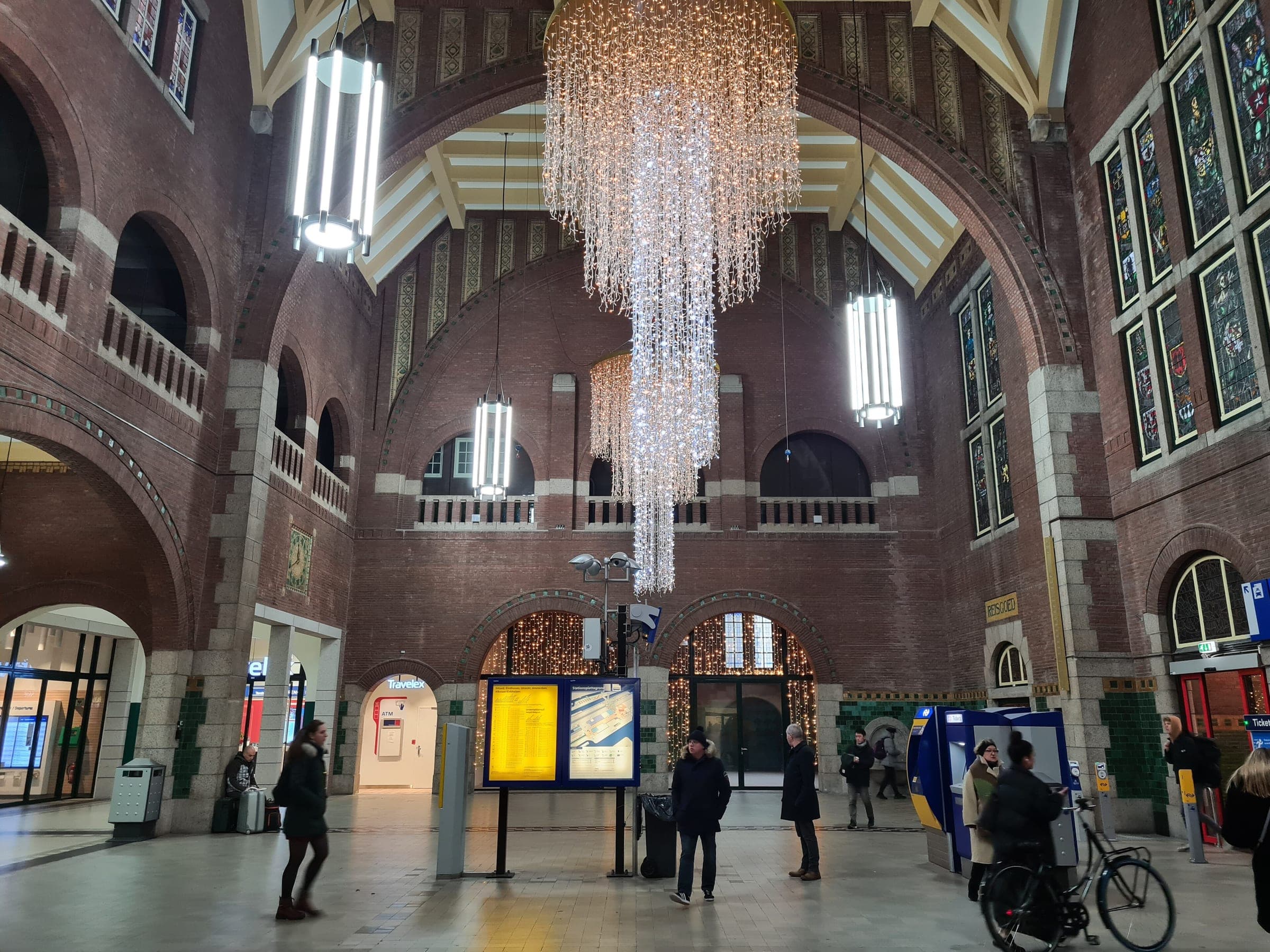 A chandelier of white lights hangs in the brick hall of Maastricht station in December.