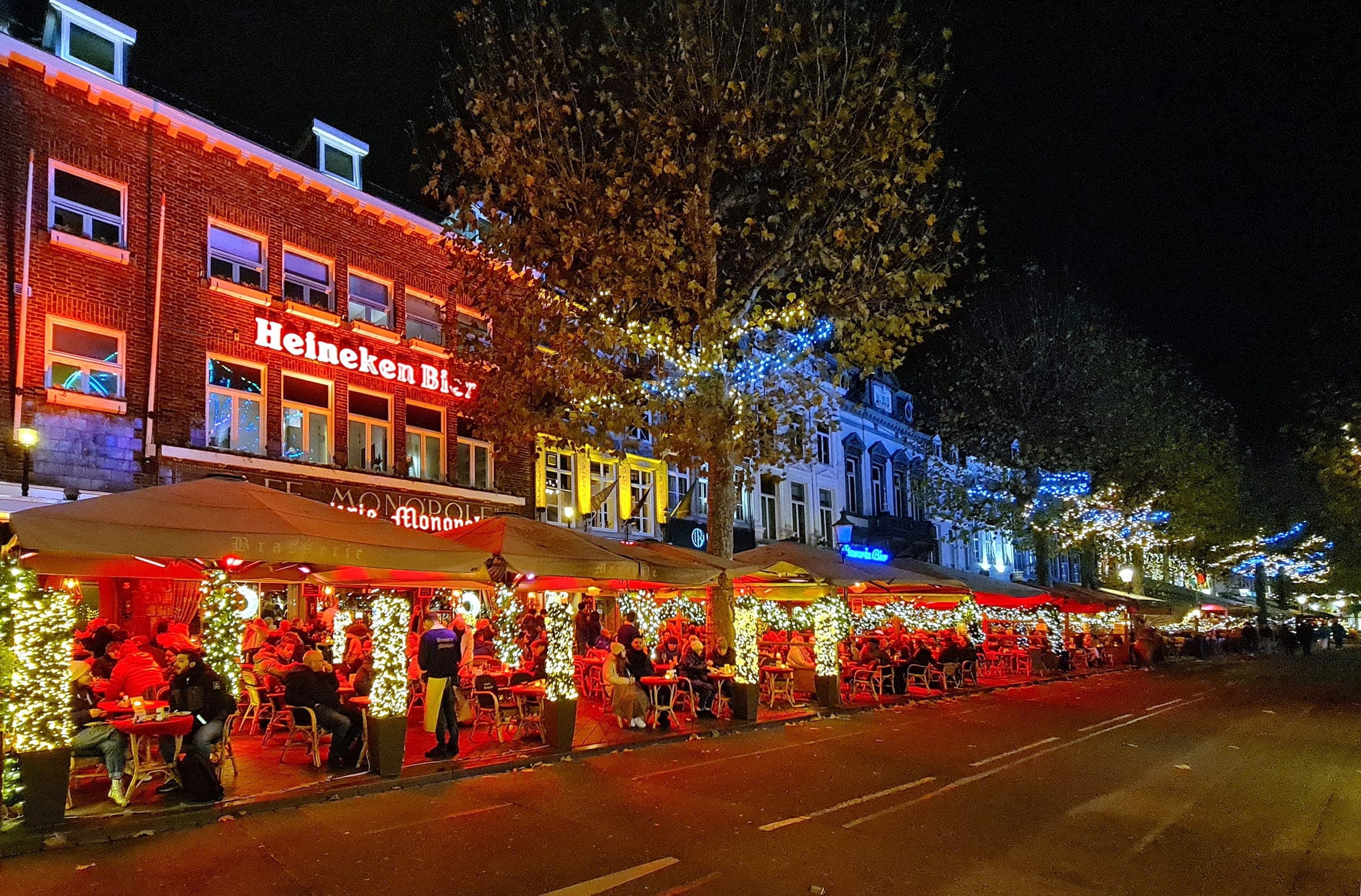 Café terraces on the Vrijthof in Maastricht glow red under strings of Christmas lights after dark.