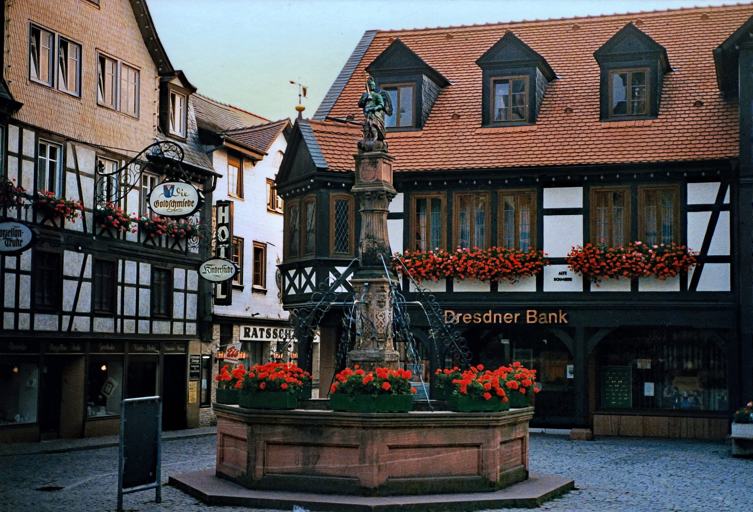 Red geraniums ring the Marktbrunnen fountain in front of timber-framed houses in Michelstadt.
