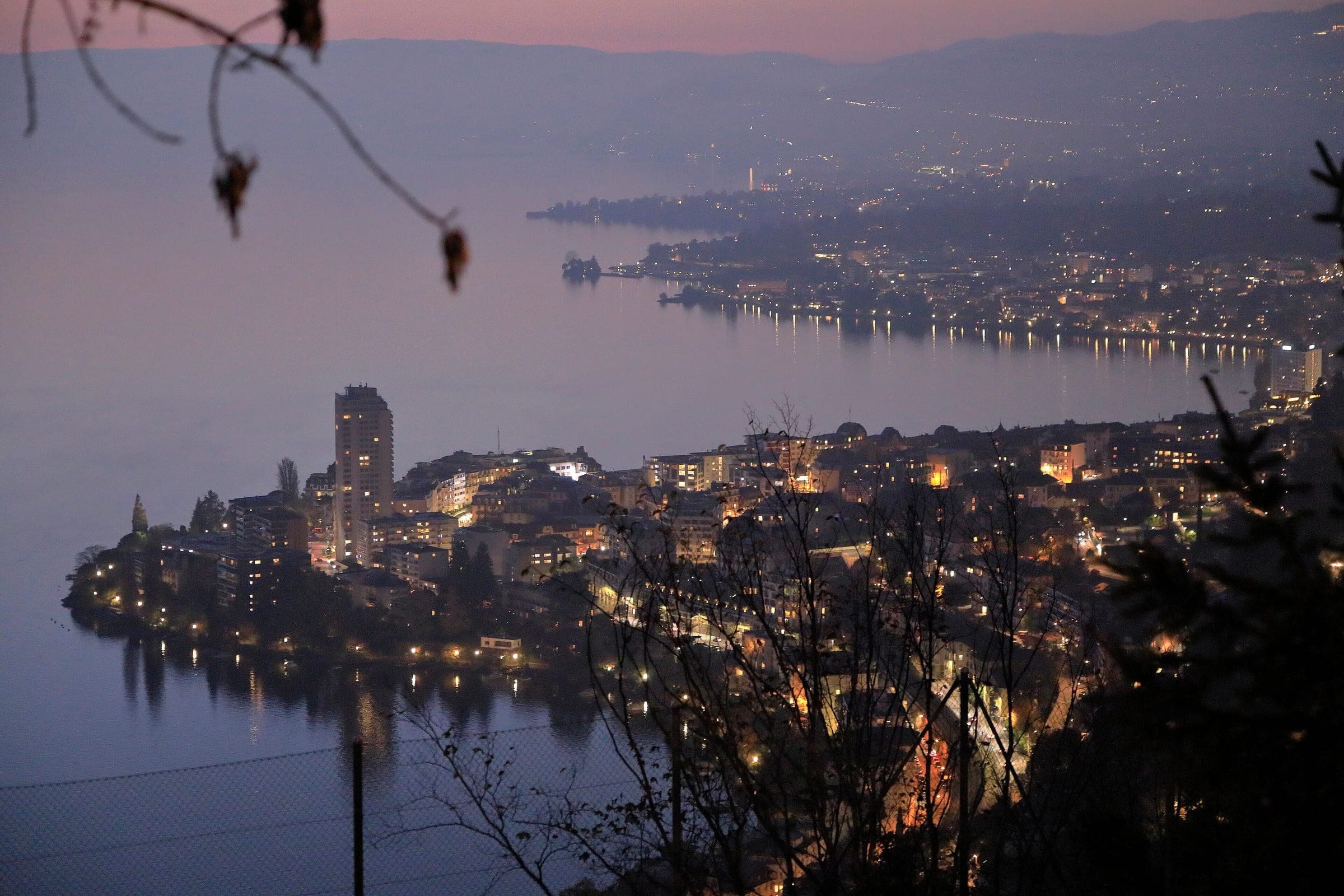 The lights of Montreux come on along the shore of Lake Geneva at dusk